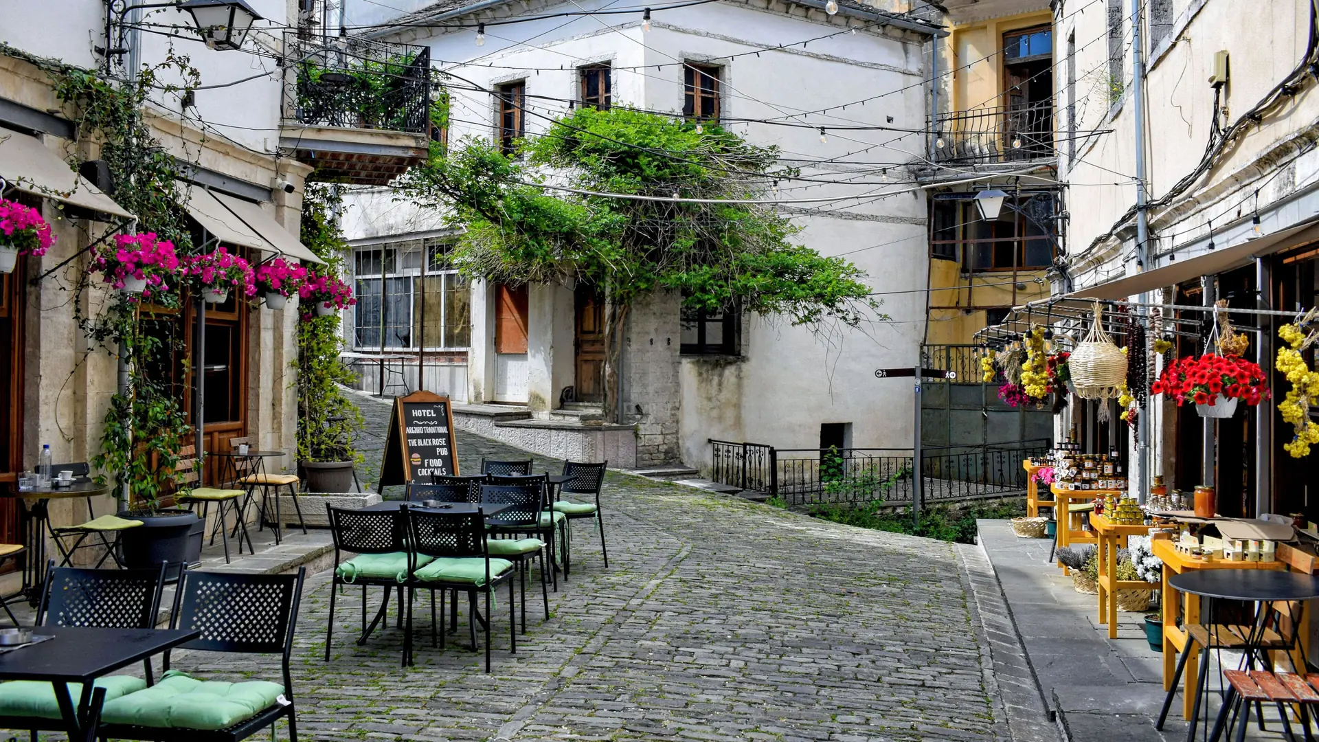 Café tables, flowers and stone houses on a cobbled street in Gjirokastër's old town
