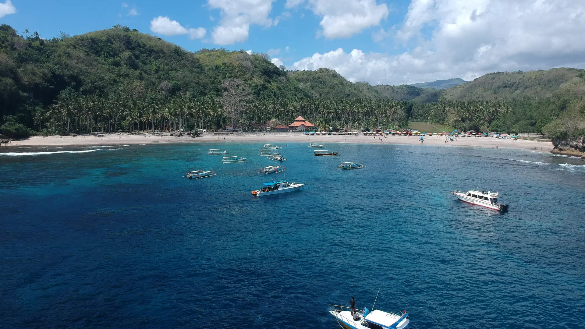 Boats on blue water in Crystal Bay below the green Nusa Penida hills