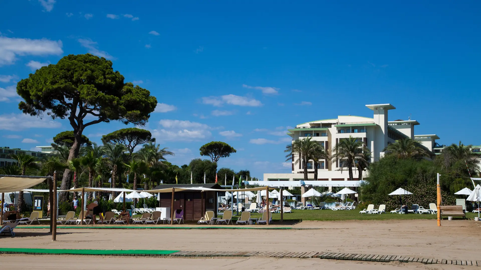 Sandy shore and pine-framed grounds at Rixos Premium Belek under a clear blue sky