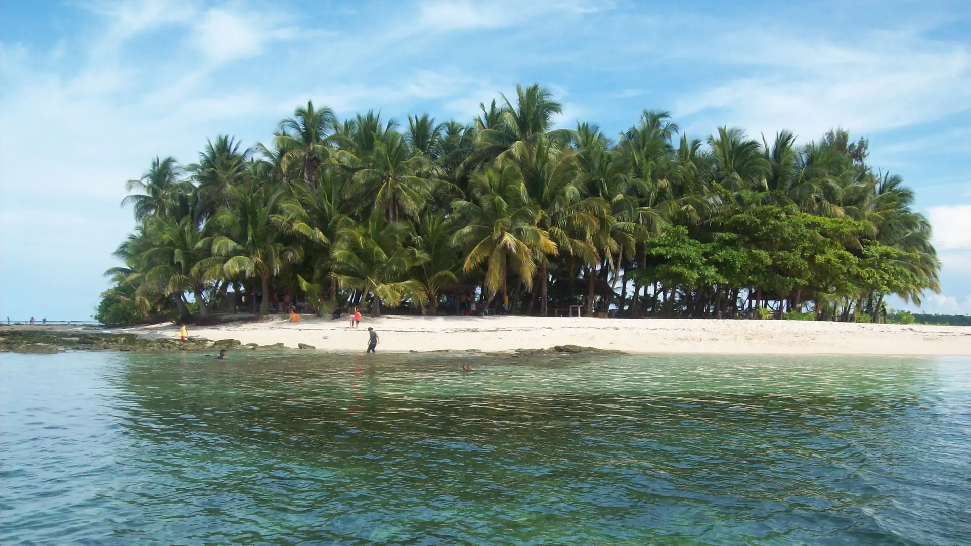 People beside the palm-lined sandy shore of Guyam Island, Siargao