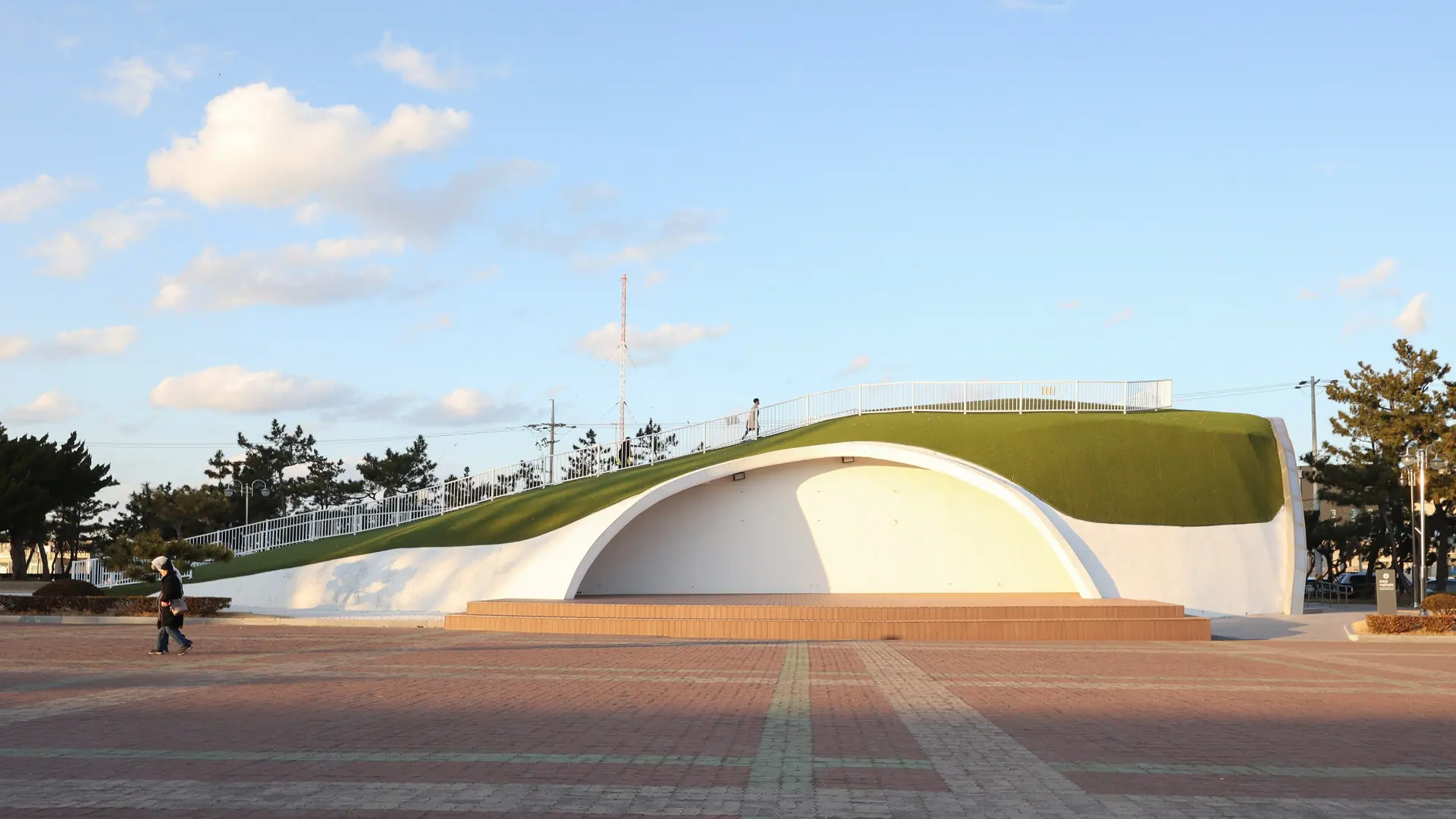 The curved grass-covered roof and paved plaza at Homigot Sunrise Square beneath a blue sky