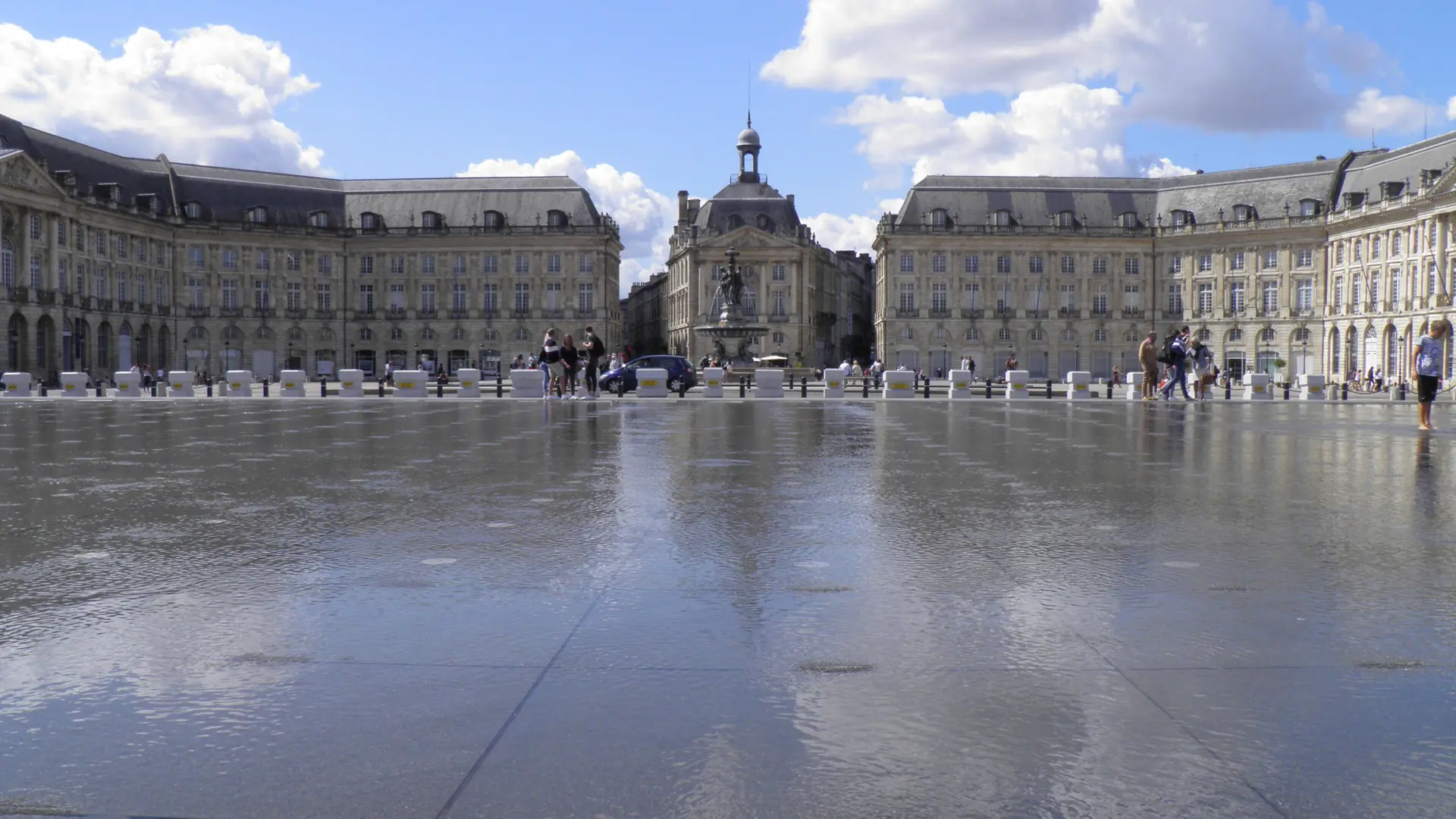 Place de la Bourse in Bordeaux and its central fountain reflected in the Miroir d’eau beneath a blue sky