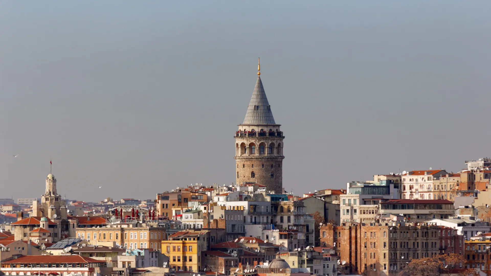 Galata Tower’s stone cylinder and conical roof above sunlit Istanbul rooftops