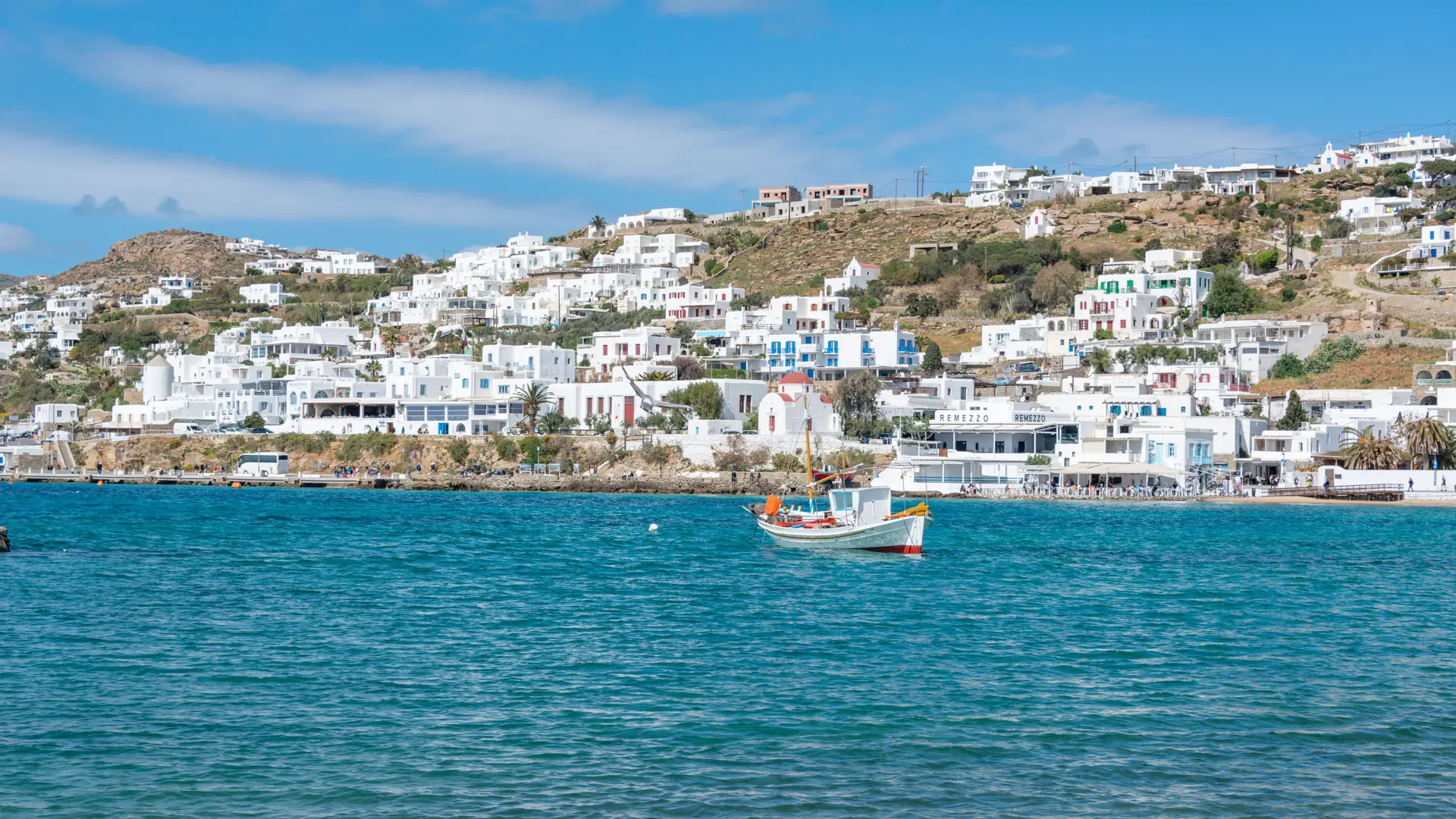 Whitewashed Mykonos Town above the blue sea, with a fishing boat crossing the bay