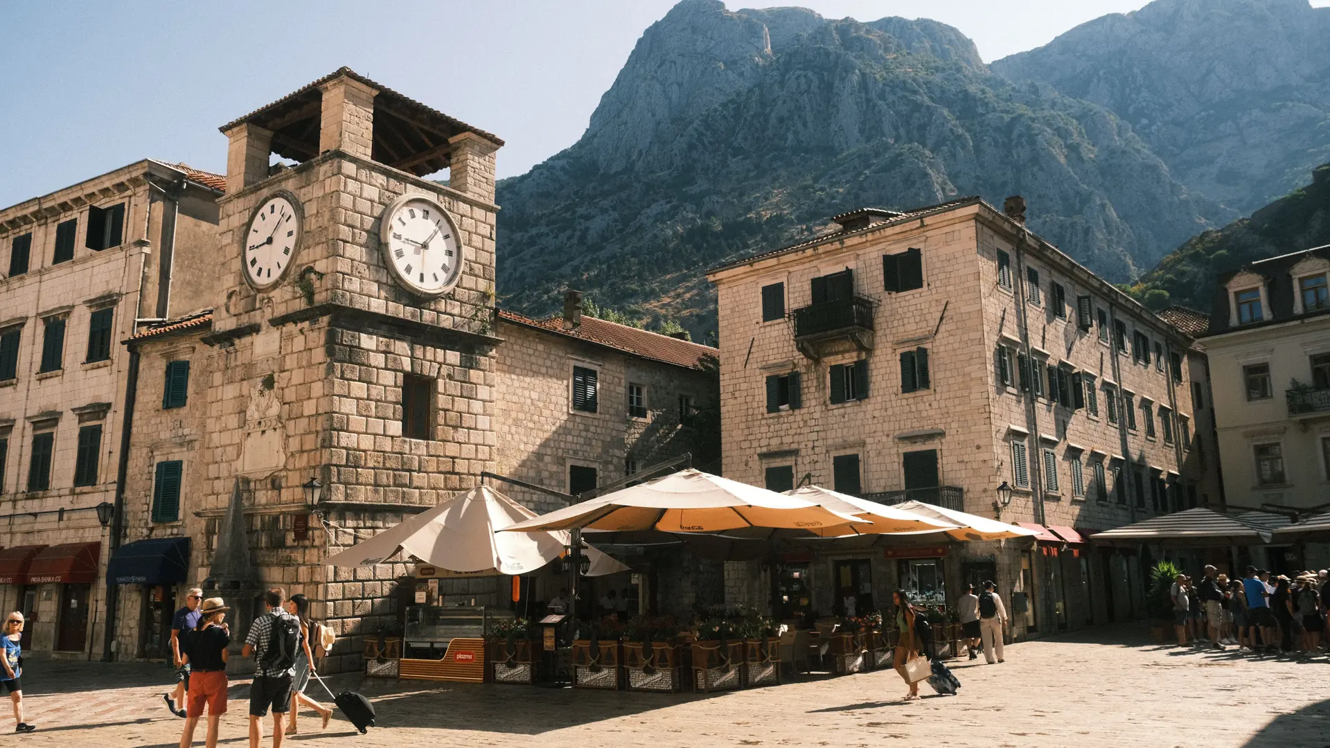 Kotor Old Town clock tower and pedestrian square beneath mountains in bright daylight