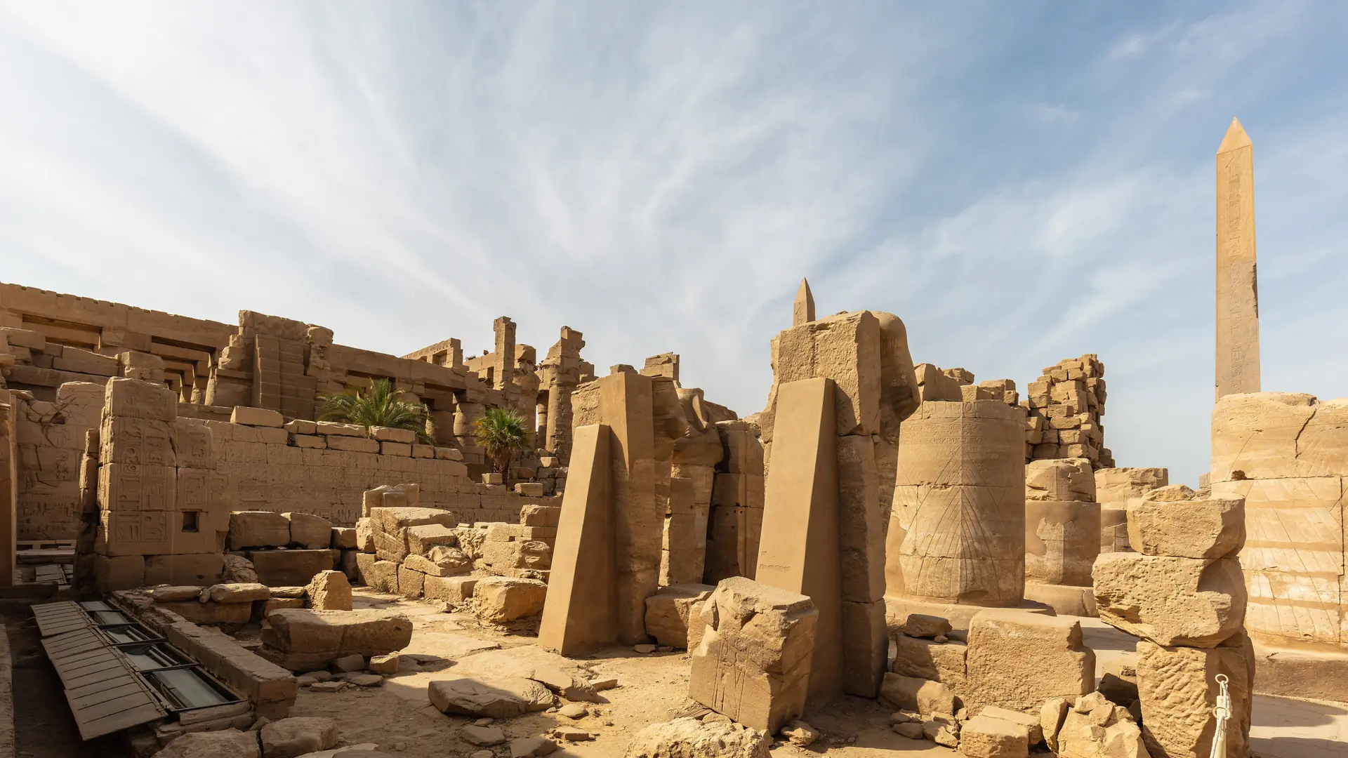Sunlit Karnak temple ruins and obelisk in Luxor beneath a blue sky.