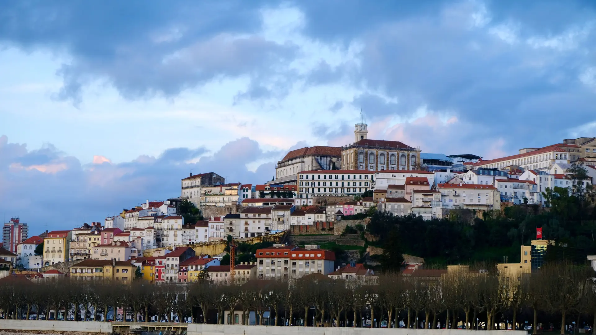 Historic Coimbra buildings rising above the river under a vivid sky