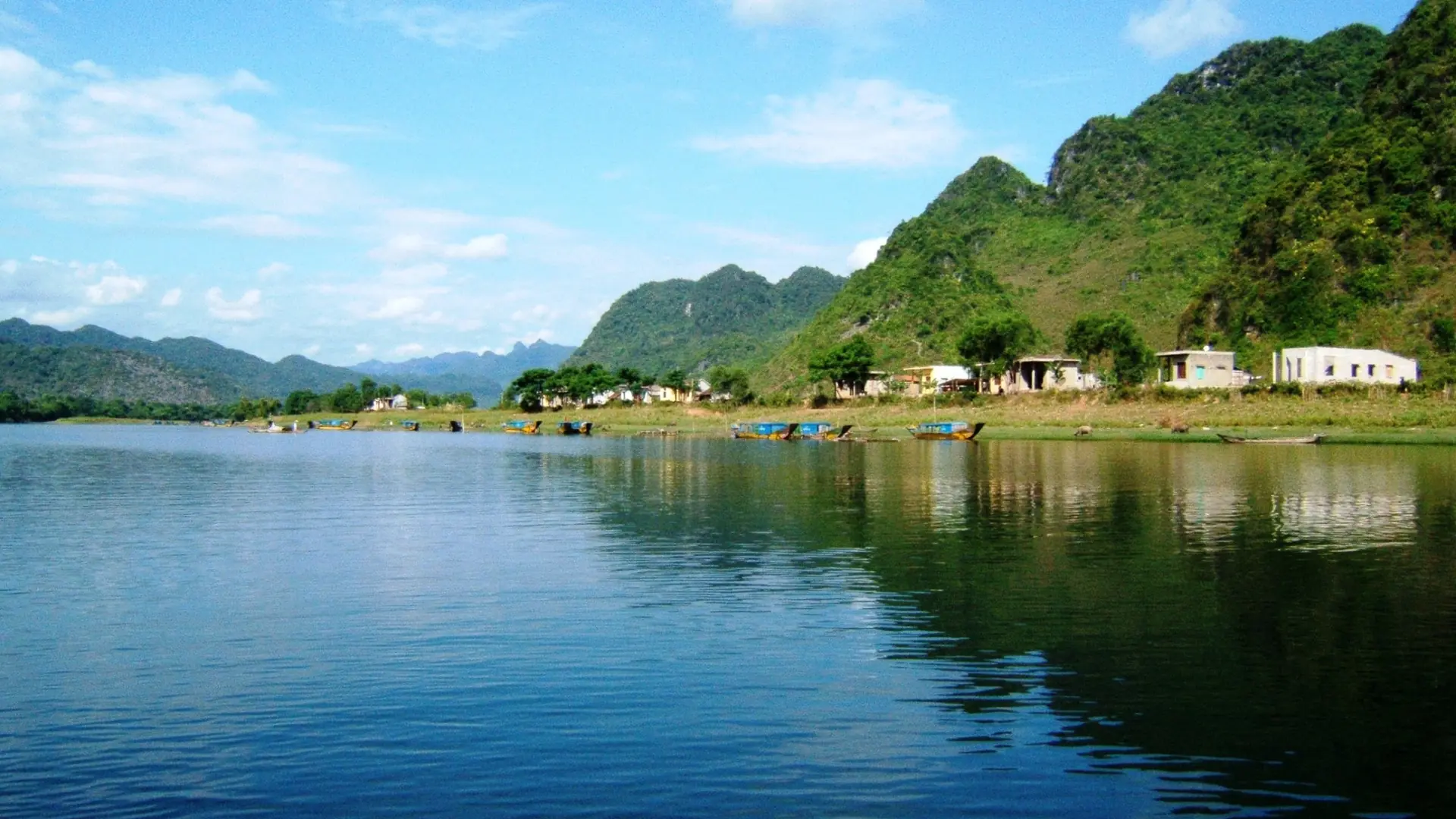 Blue water and wooded limestone hills along the Son River on the approach to Phong Nha Cave