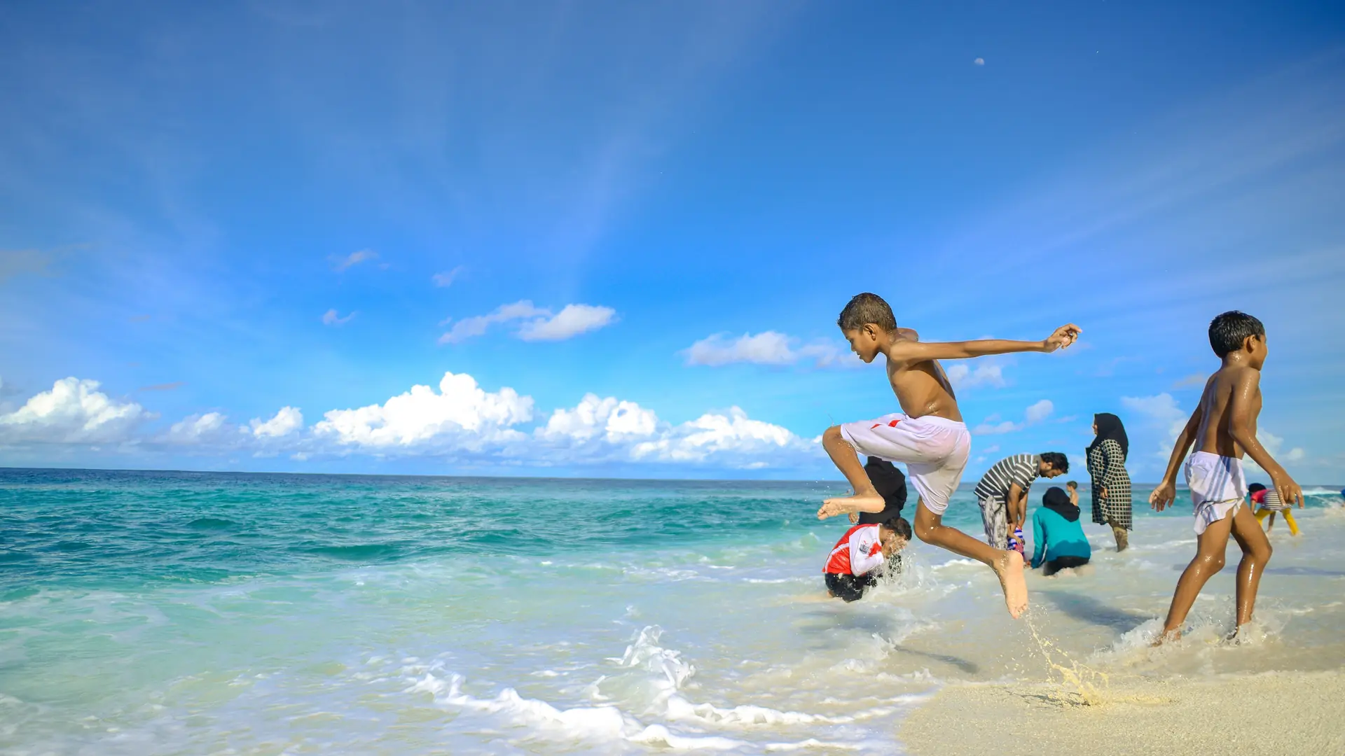 Children splashing in shallow blue water on a Maldivian beach in daylight