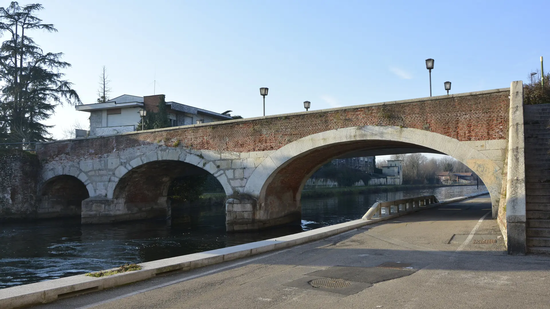 a brick-arched bridge over the Naviglio Grande canal in Milan under a clear sky