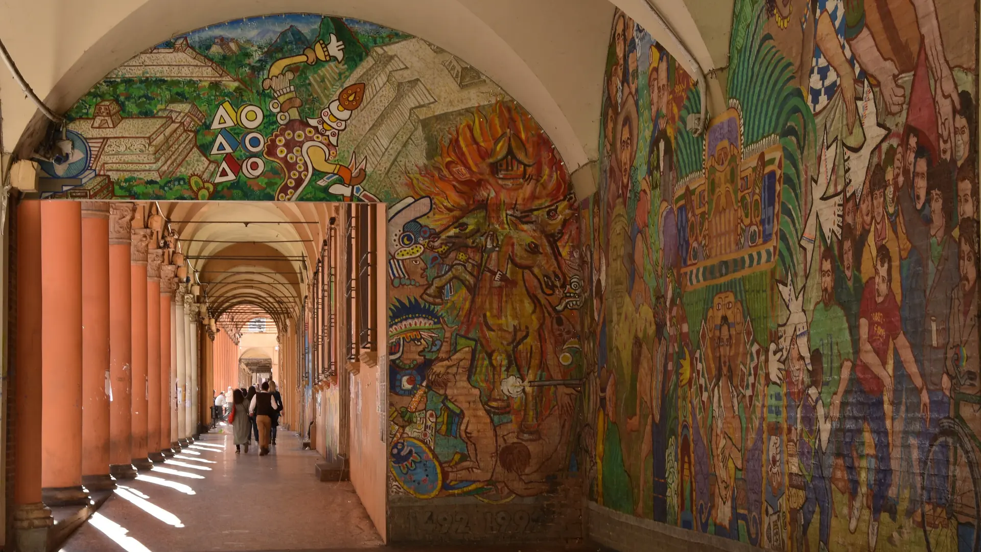 a sunlit mural-covered portico near the university in Bologna
