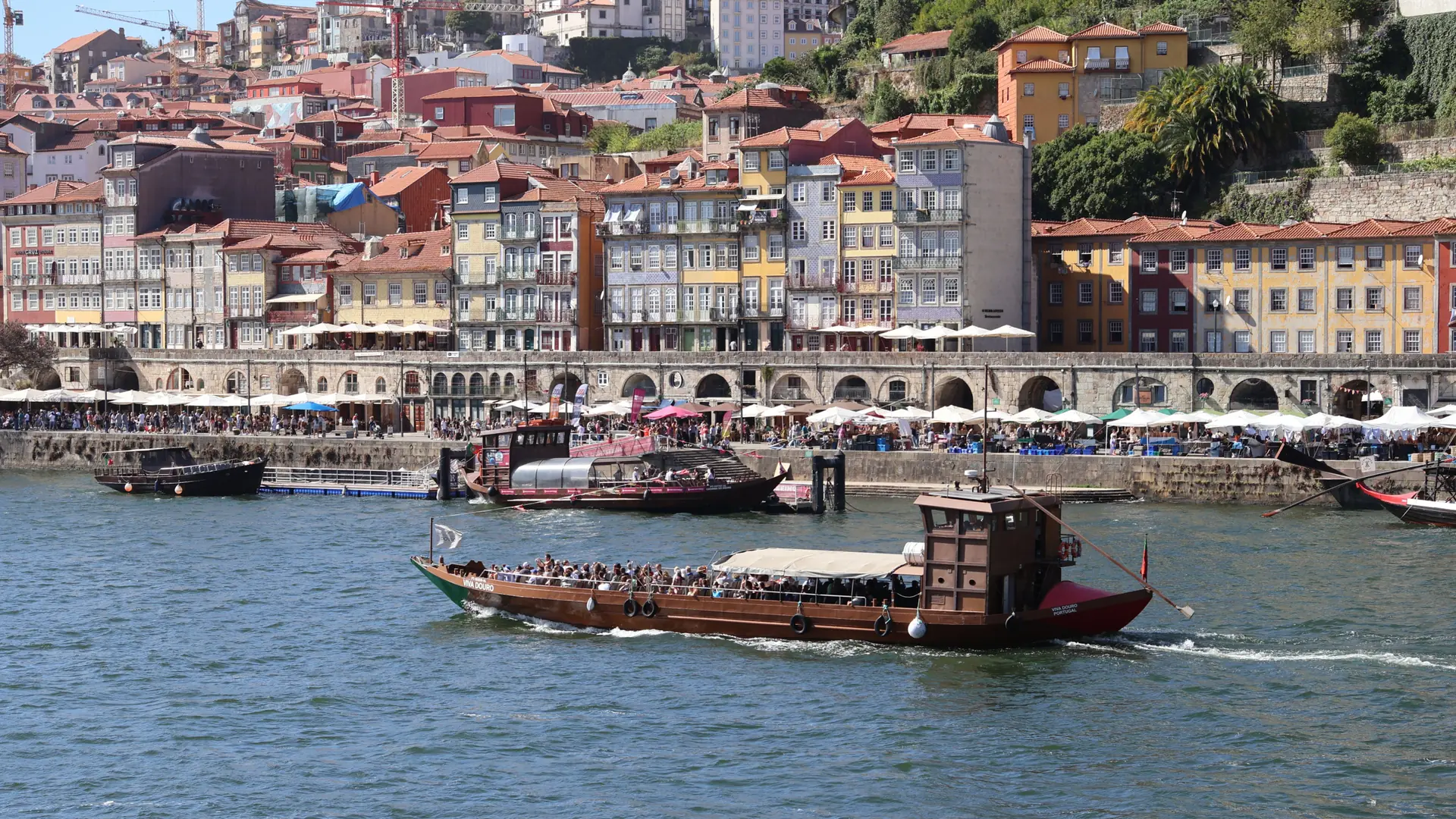 sunlit colourful façades along Porto's Ribeira waterfront, with boats on the Douro