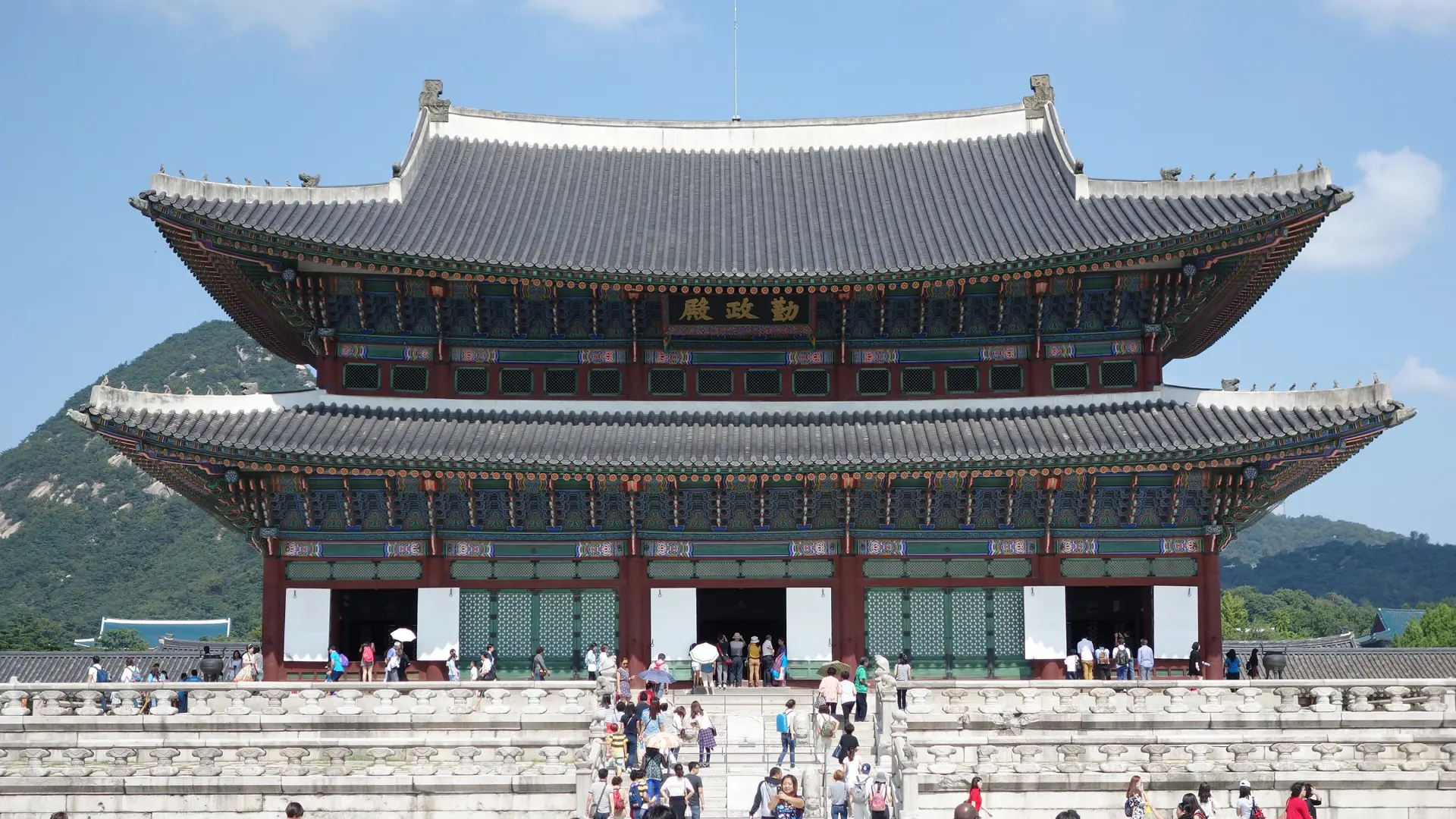 Gyeongbokgung Palace's Geunjeongjeon throne hall with its layered tiled roof under a bright blue sky, Seoul