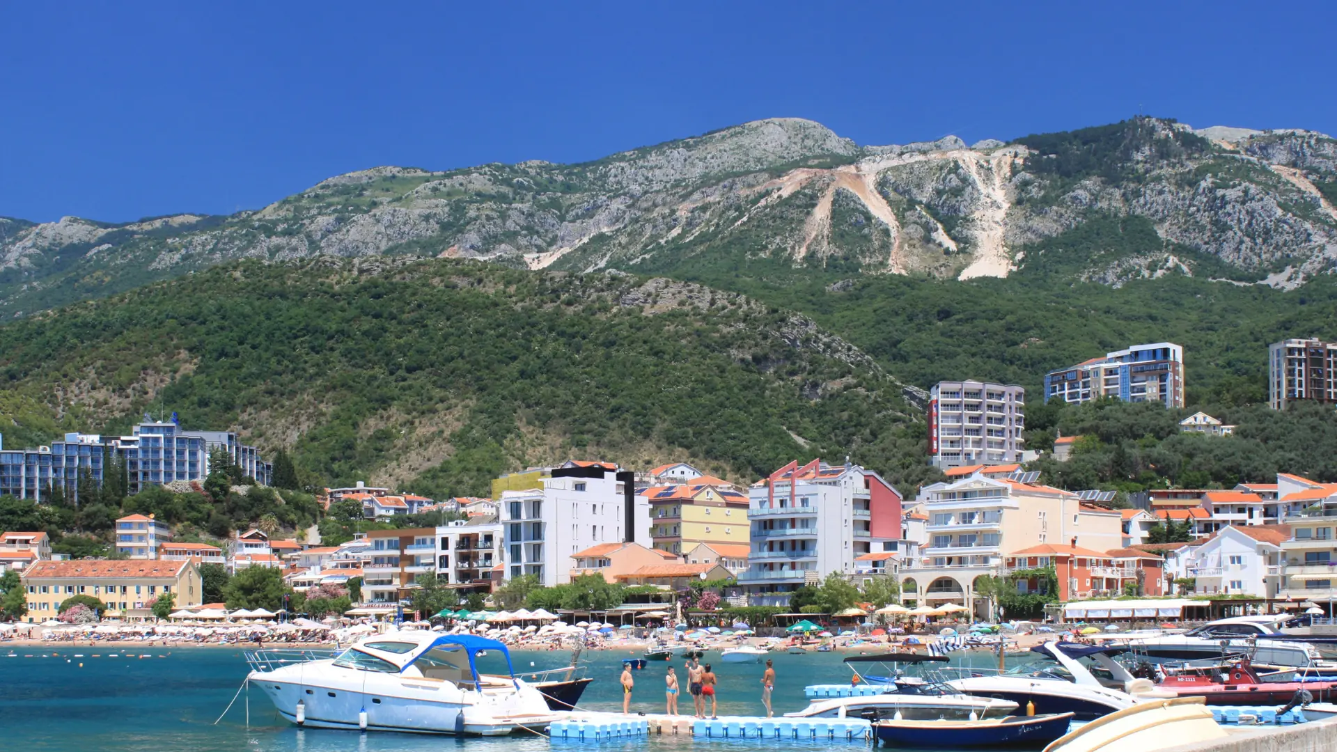 Fishing boats off the Rafailovići waterfront, with village buildings and green hills behind