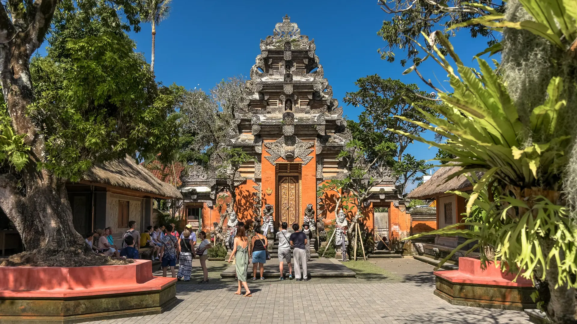Visitors beside the carved stone and orange gateway of Puri Saren Agung Ubud Palace