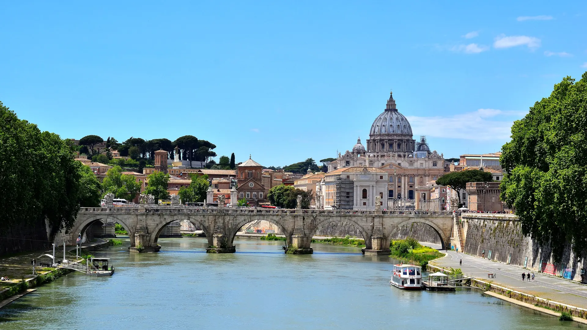 St Peter's Basilica dome rising beyond Ponte Sant'Angelo over the Tiber under a clear blue sky
