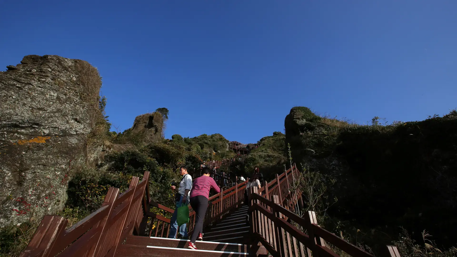 Visitors climb wooden steps between the volcanic rocks of Seongsan Ilchulbong on Jeju