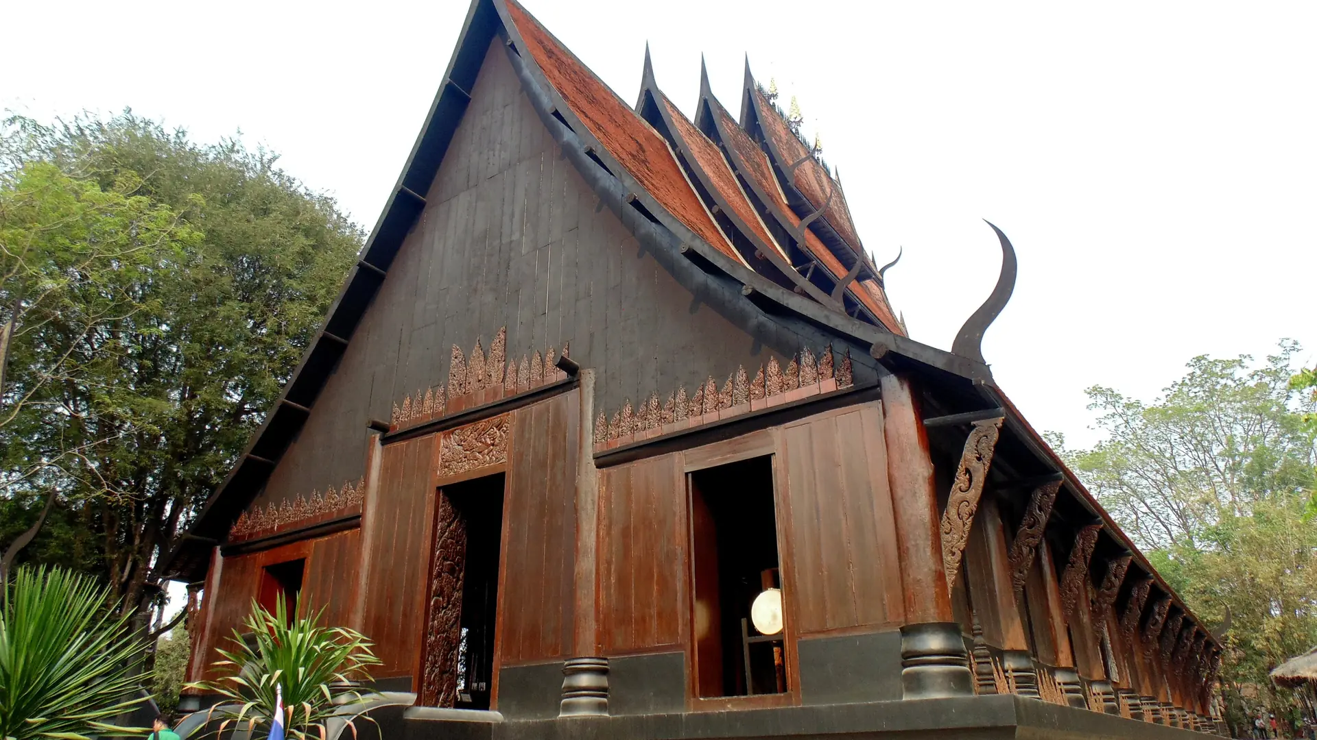 A dark timber hall with a steep Lanna roof at Chiang Rai's Baan Dam Museum