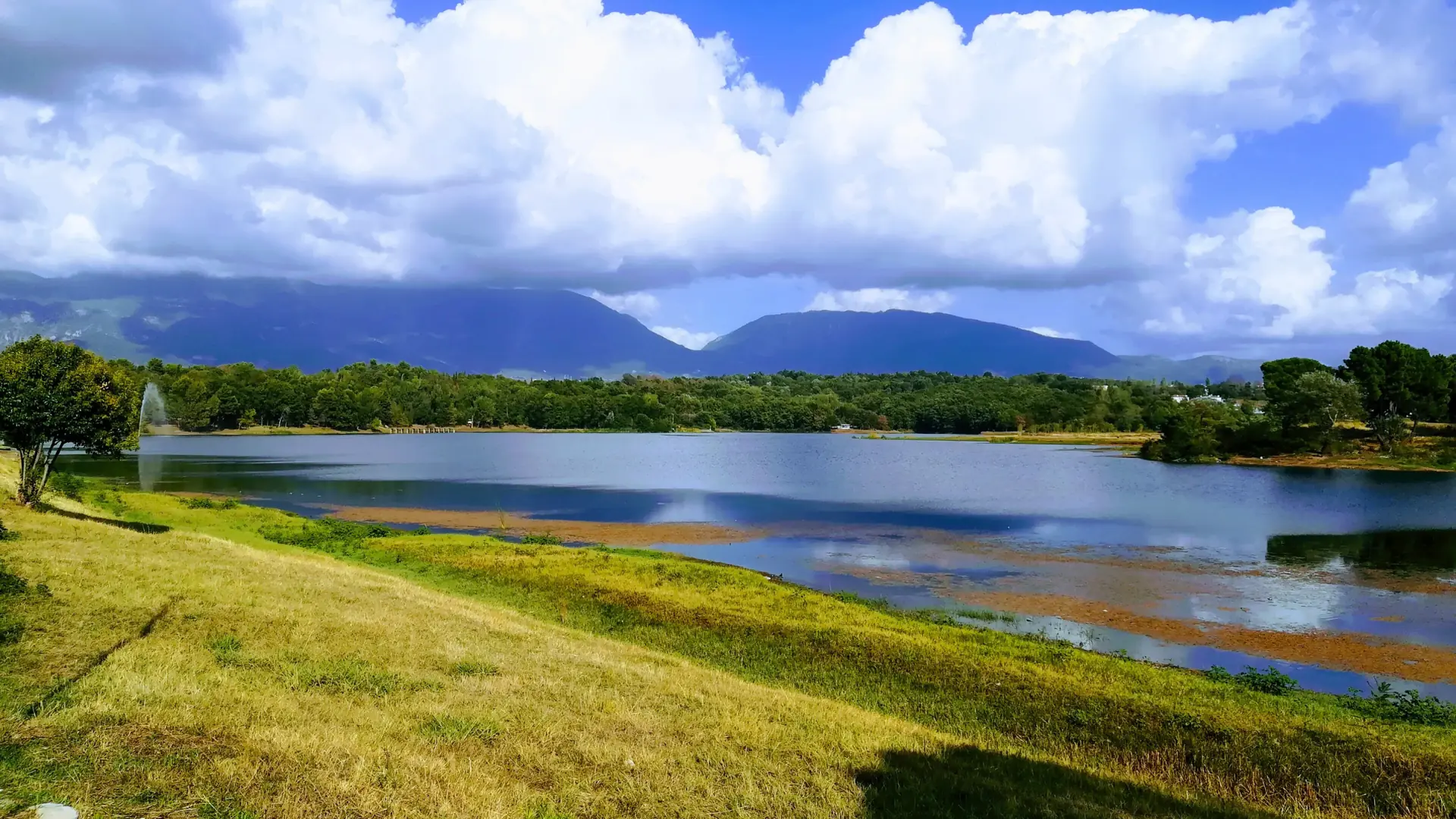 The Artificial Lake in Tirana's Grand Park, with green lawns and mountains under a bright sky