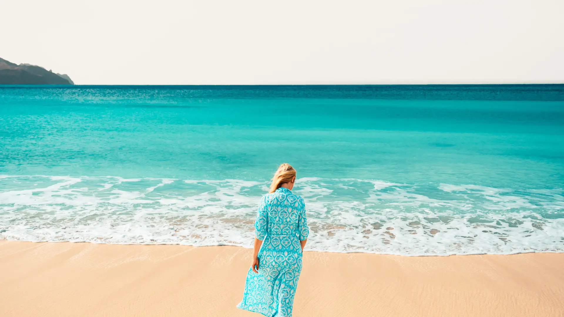Woman standing at the turquoise shoreline of Praia da Laginha in Mindelo