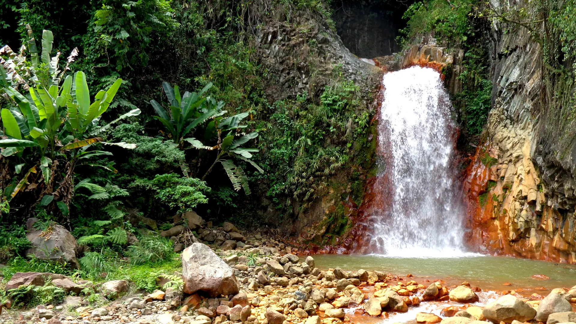 Pulangbato Falls dropping through a dark cleft onto rust-red rocks near Valencia