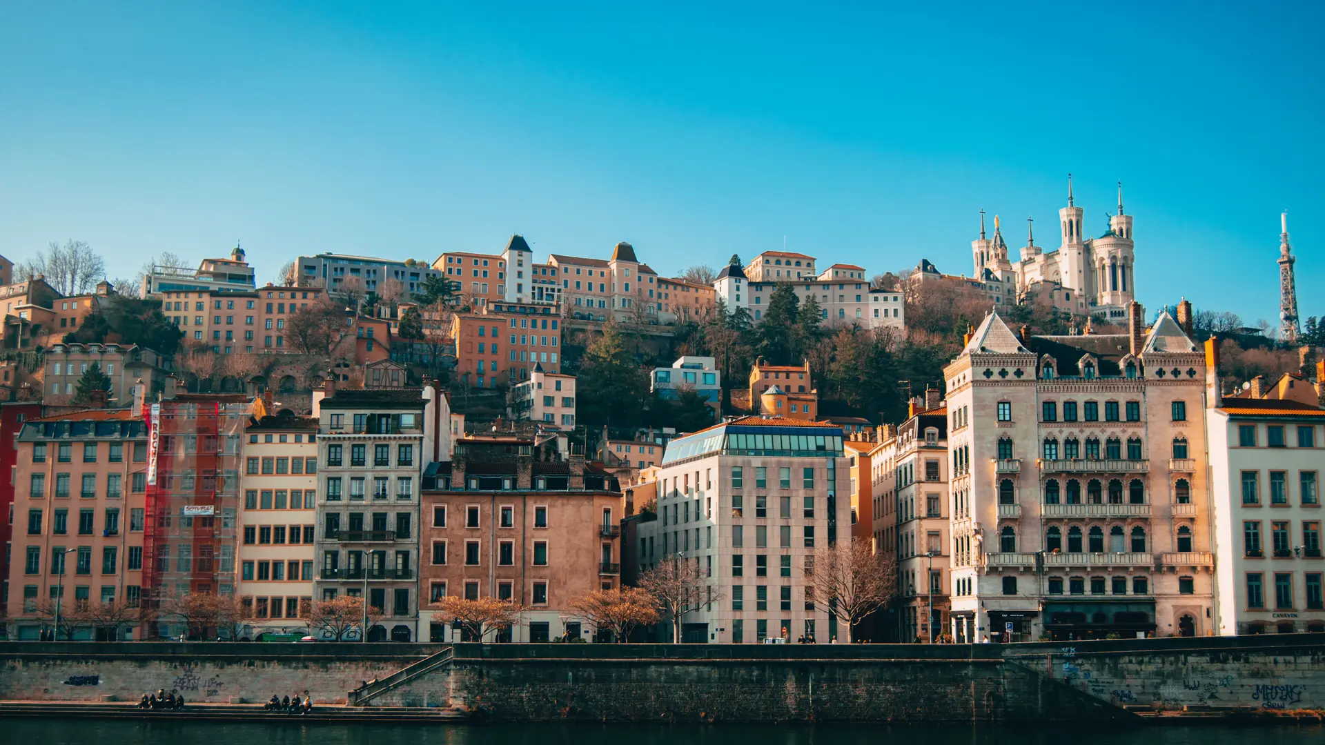 Sunlit buildings beside the Saône below Fourvière in Lyon, shown as a wider city scene