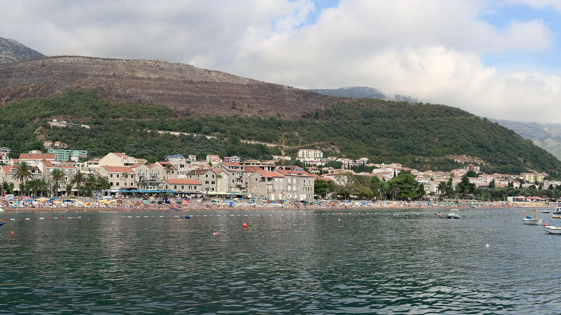 Petrovac waterfront across the bay, with wooded hills rising behind the town