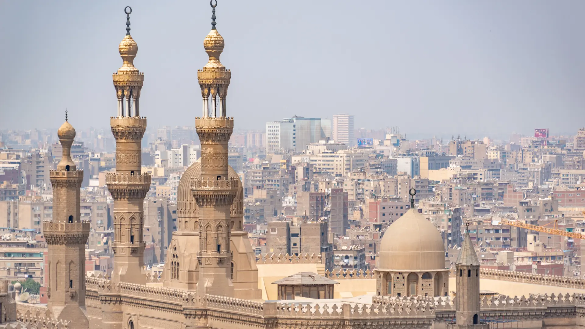 Sunlit mosque minarets and domes above dense Cairo rooftops.