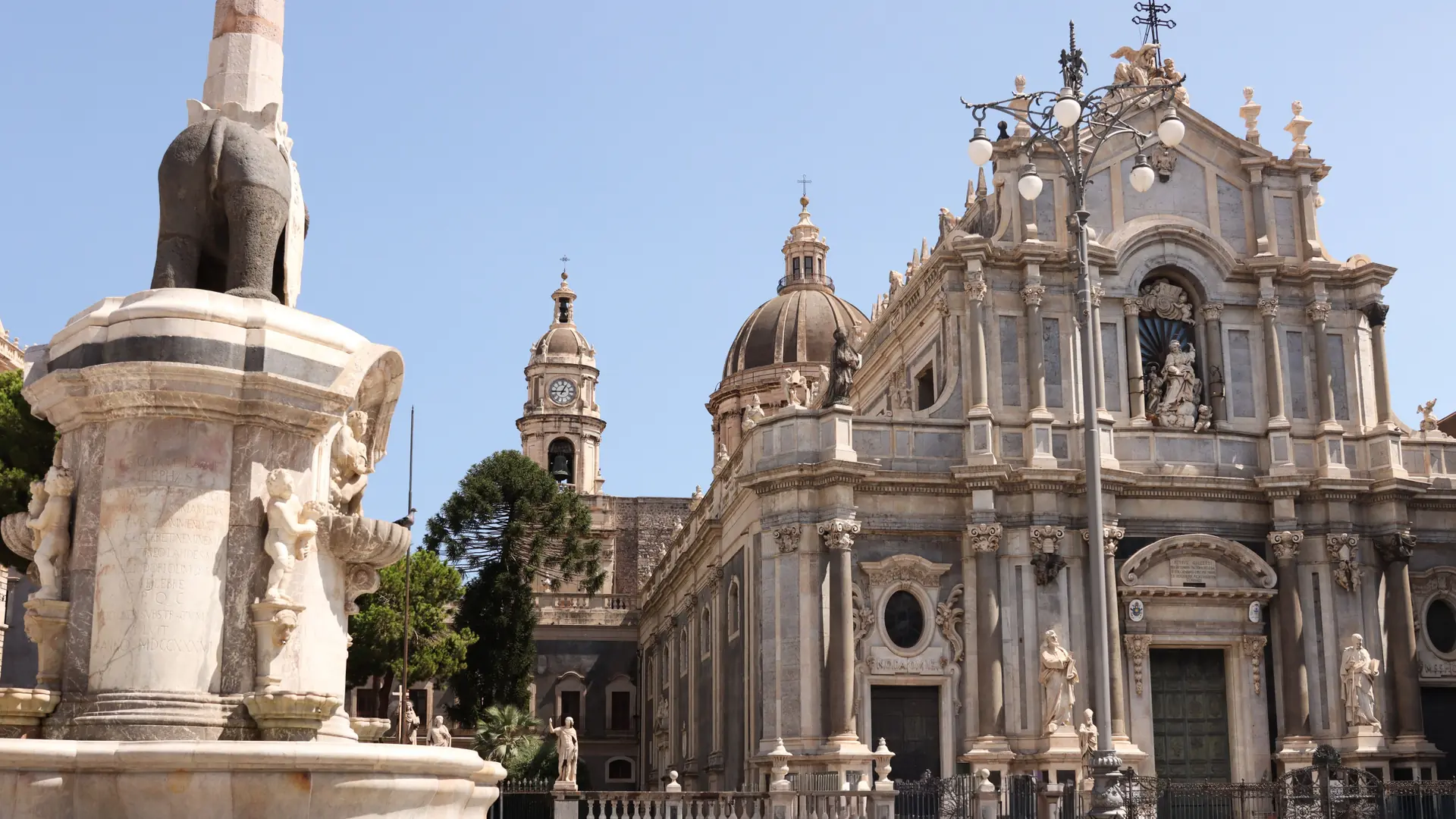Catania Cathedral and the elephant fountain in Piazza del Duomo in daylight.