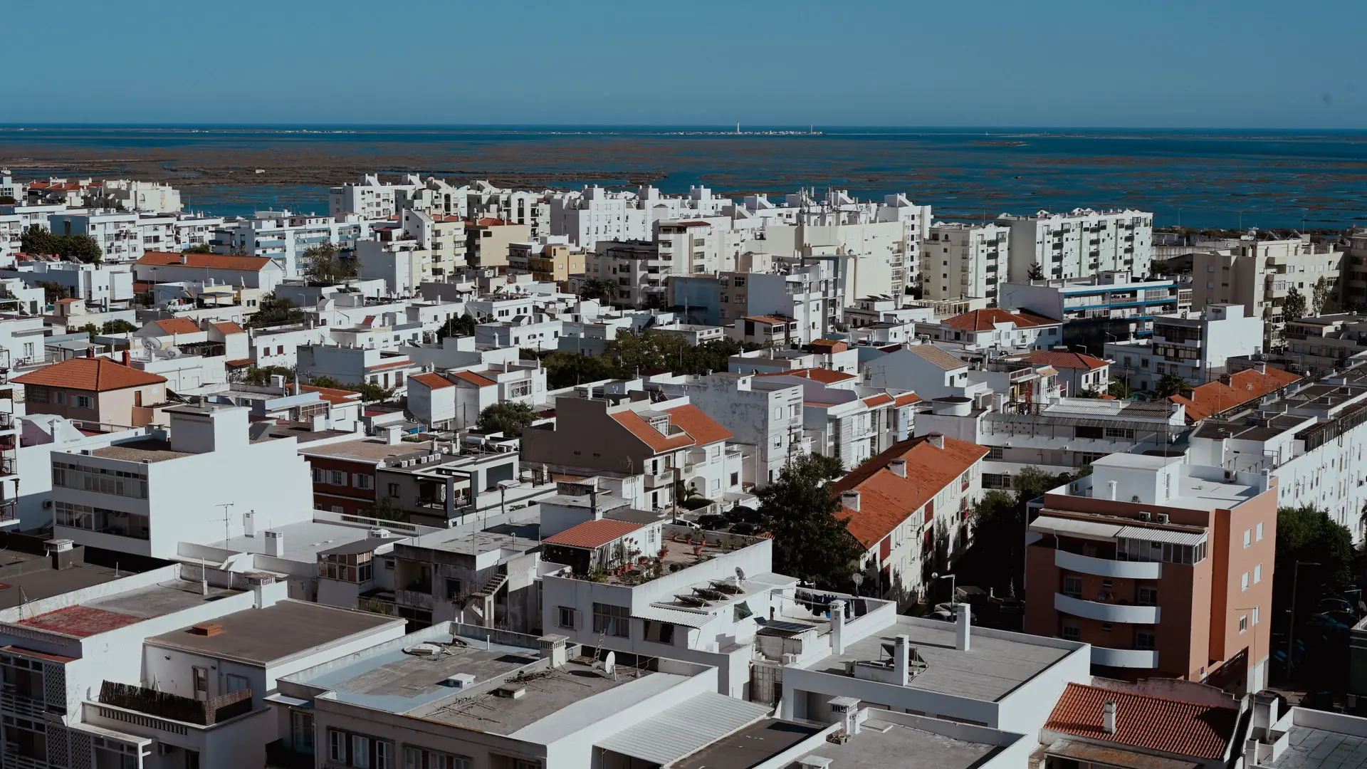 Sunny aerial view across Faro apartment roofs toward the blue Atlantic horizon