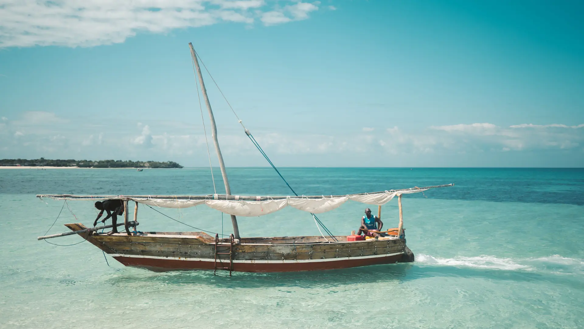 Traditional dhow crossing clear Zanzibar water beneath a bright blue sky