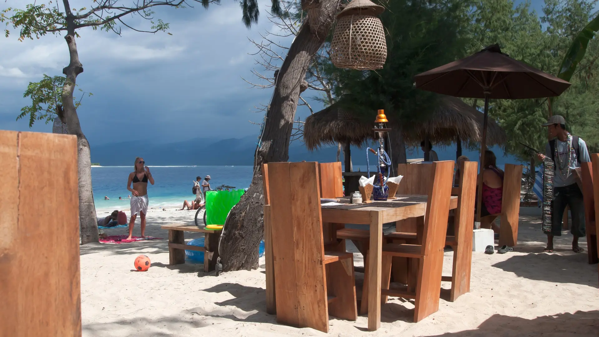 Outdoor beach café on Gili Trawangan with wooden chairs, a parasol and turquoise sea beyond