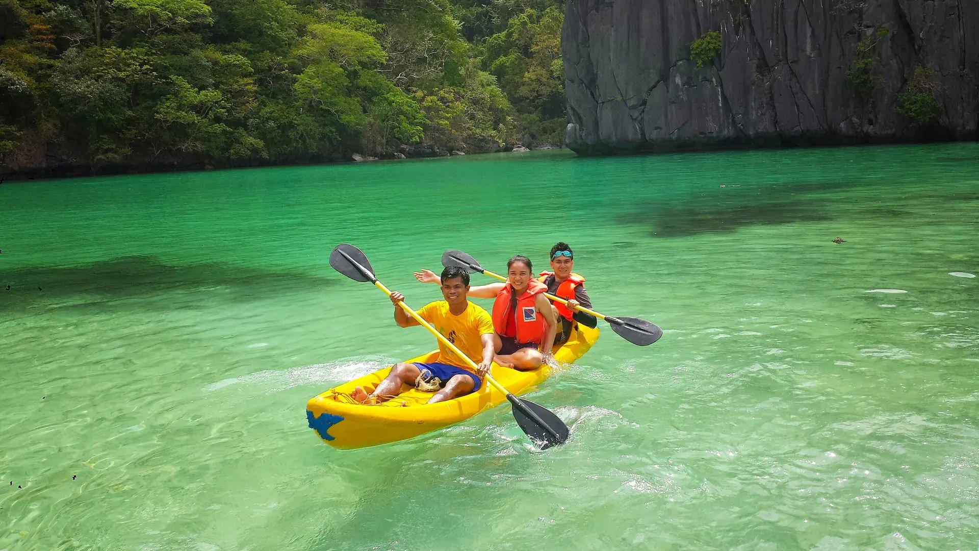 Kayakers in green water beneath the limestone cliffs of Cadlao Island, across the bay from El Nido