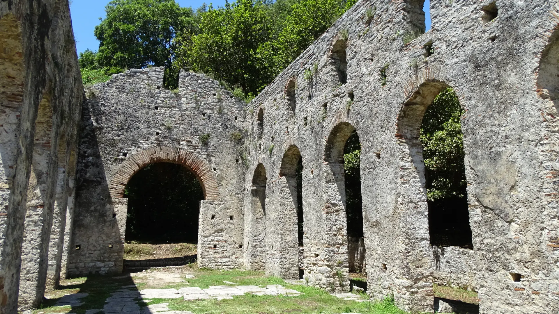 Stone and brick arches of the ruined basilica at Butrint among green trees