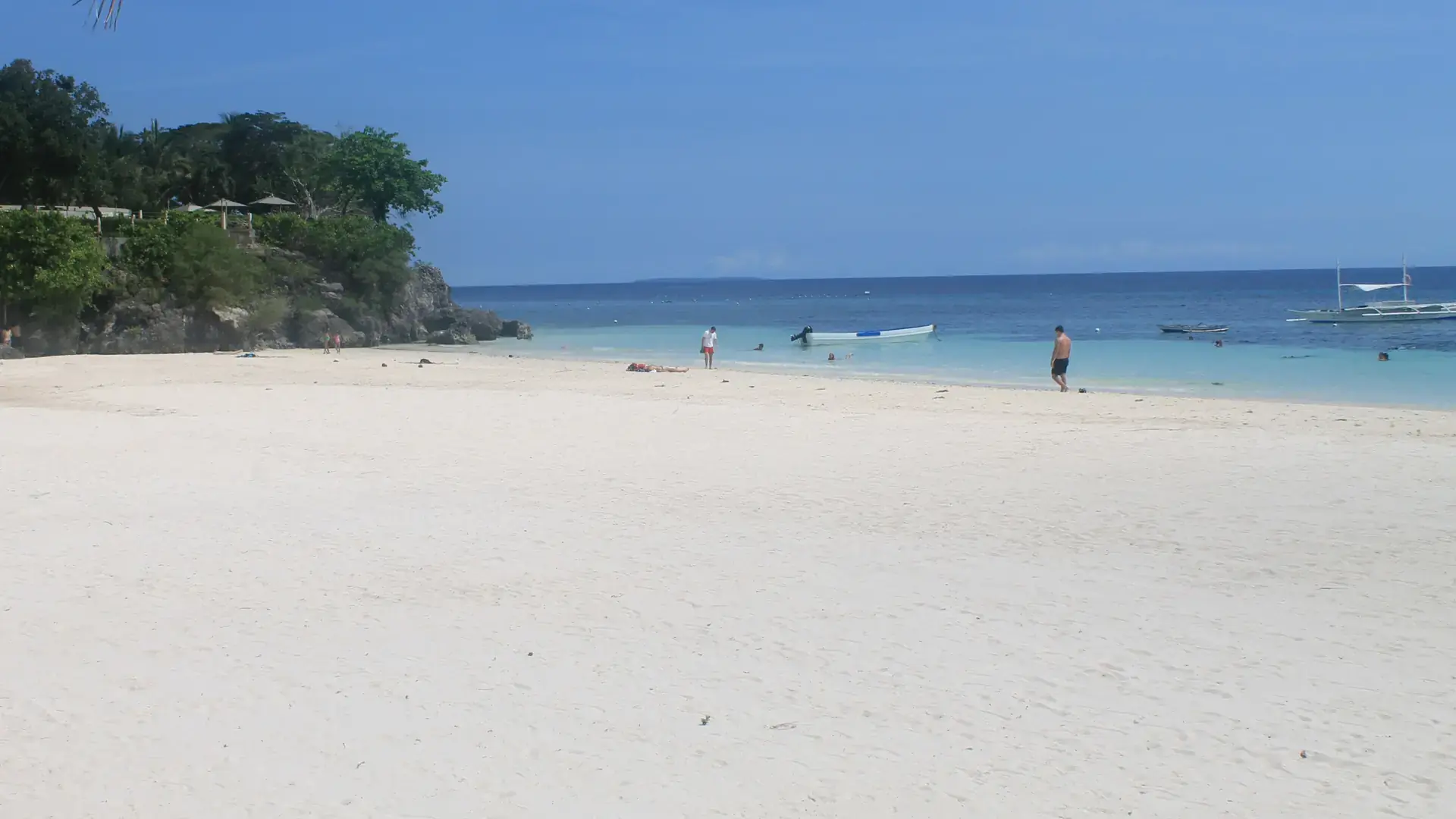 White sand and shallow sea beside the rocky end of Alona Beach on Panglao