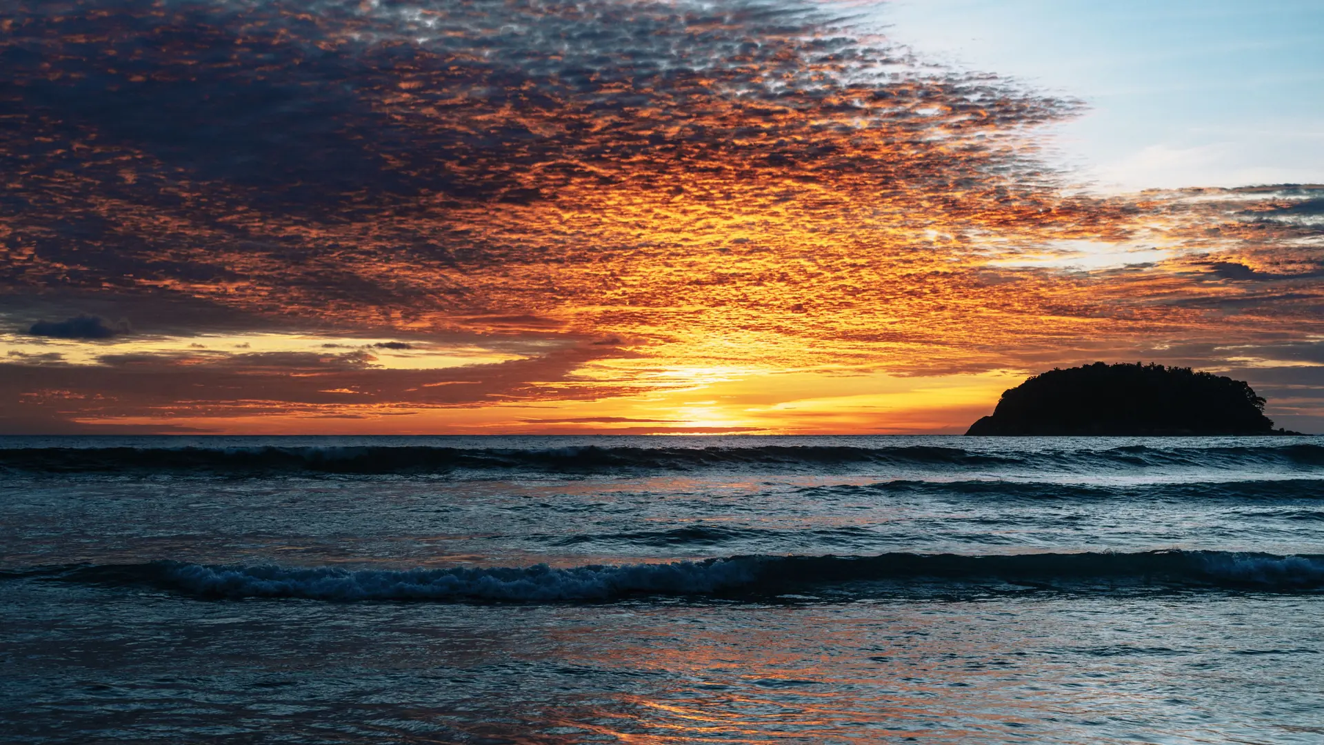 Orange sunset light reflecting across the waves at Kata Beach