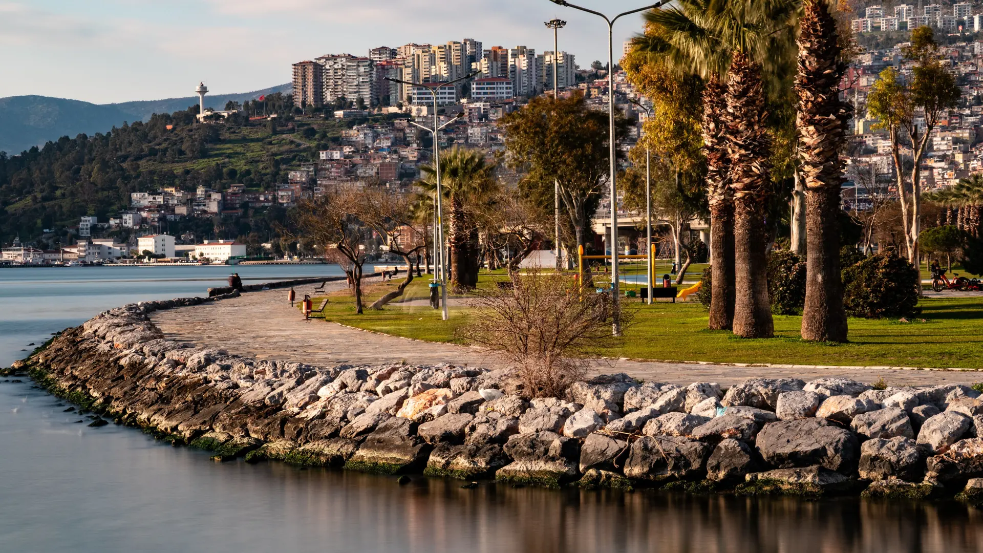 Sunny İzmir waterfront with green parkland and city buildings beside the bay