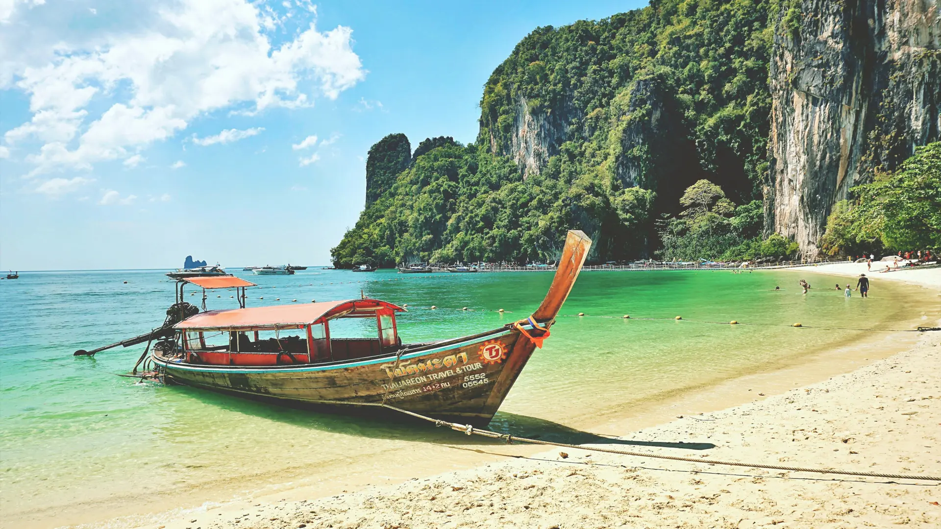 A long-tail boat floating below Railay's sunlit limestone walls