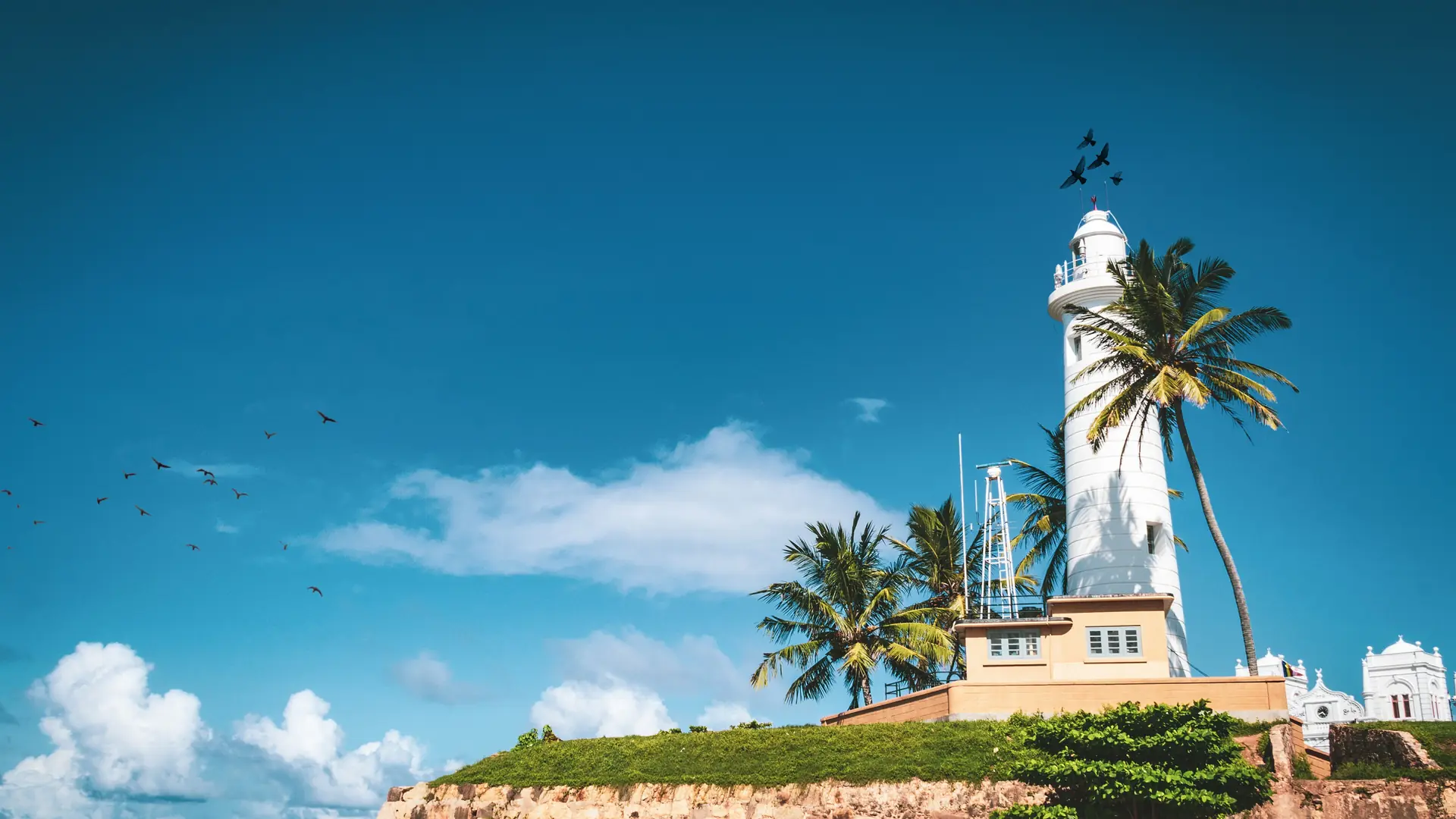White Galle Lighthouse above a grassy fort rampart beneath a blue sky