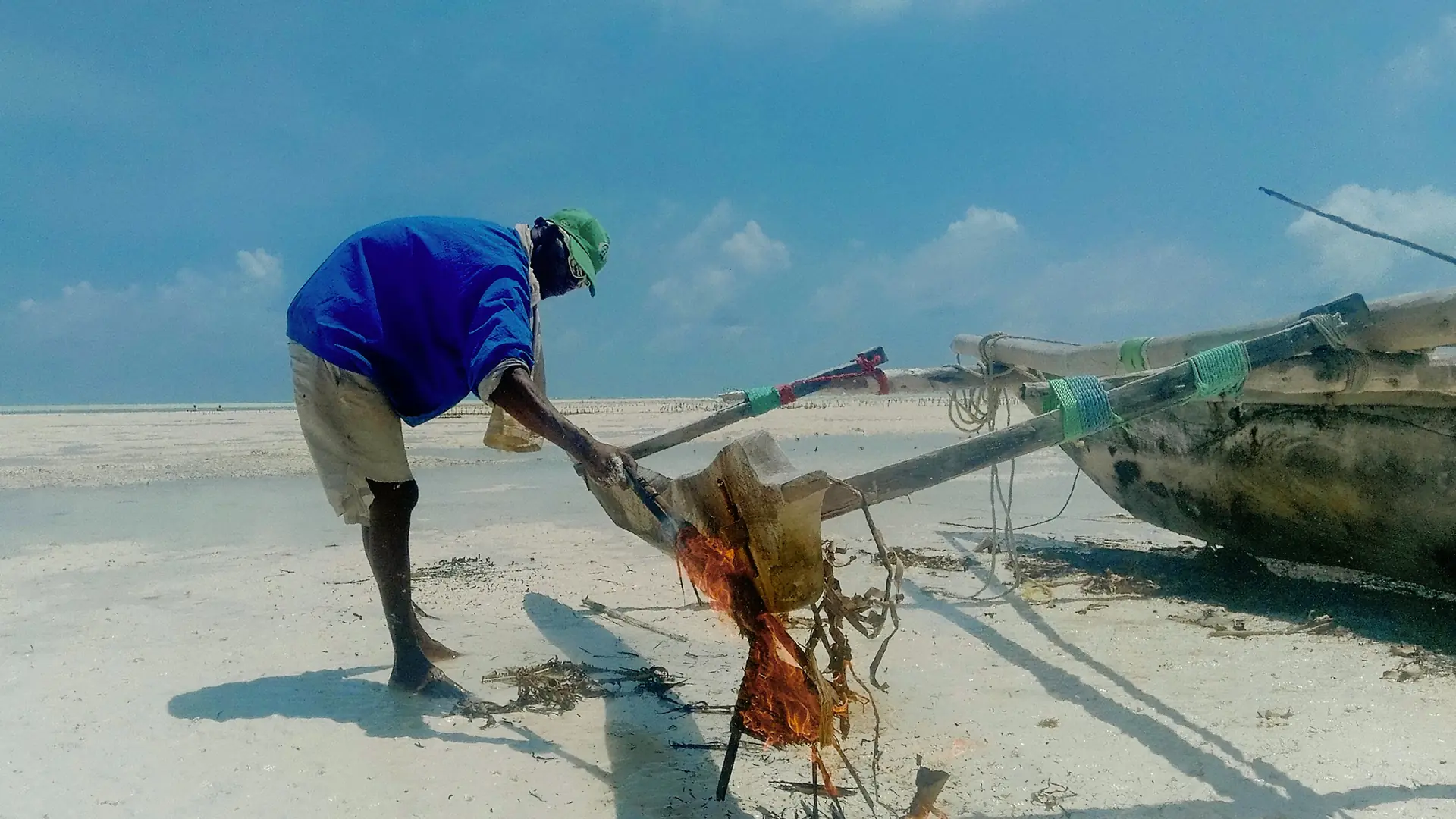 Fisherman maintaining a wooden dhow on the sunlit shore at Jambiani, Zanzibar