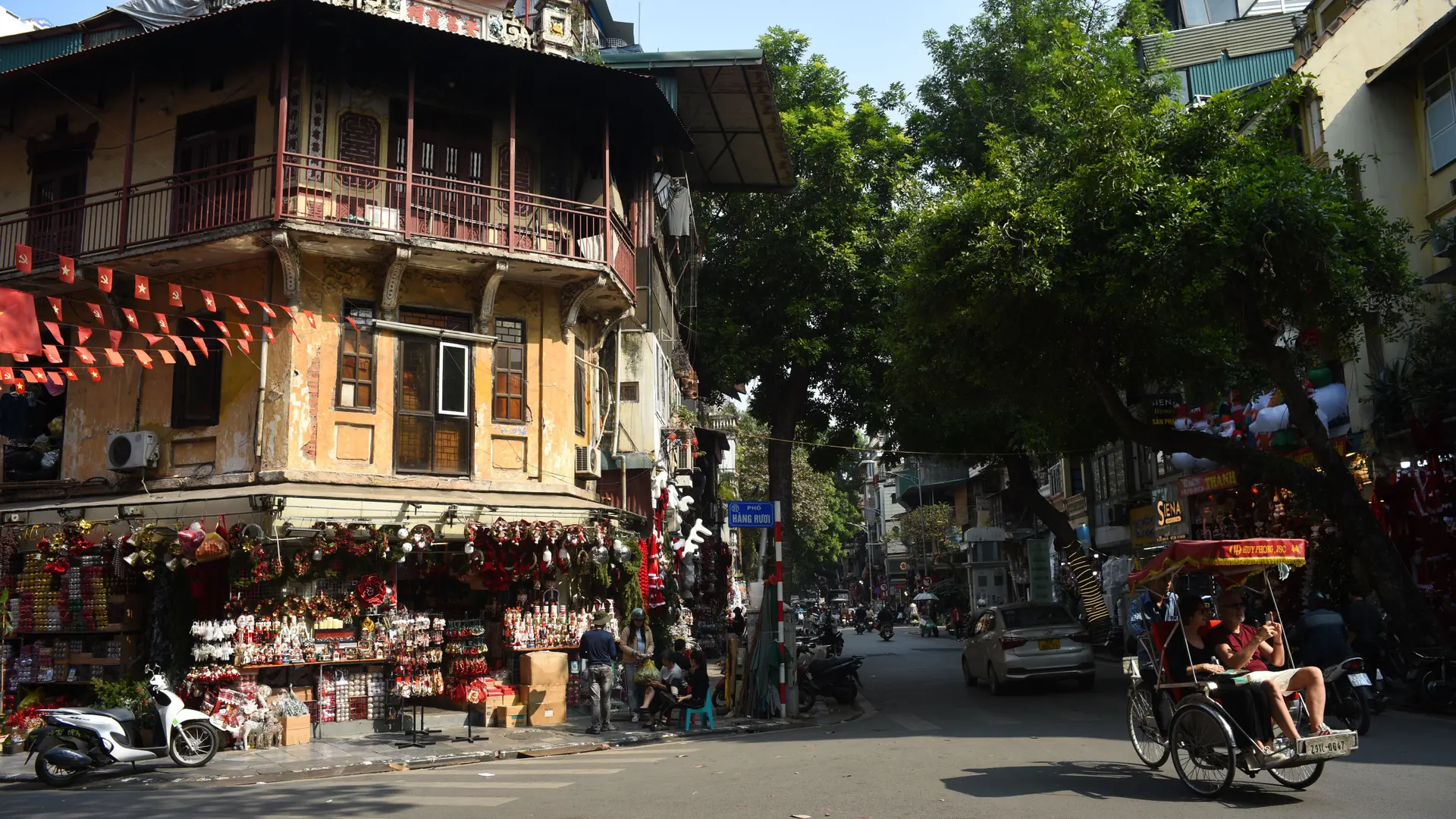 Cyclo passing a decorated corner building on Hang Ruoi in Hanoi’s Old Quarter.