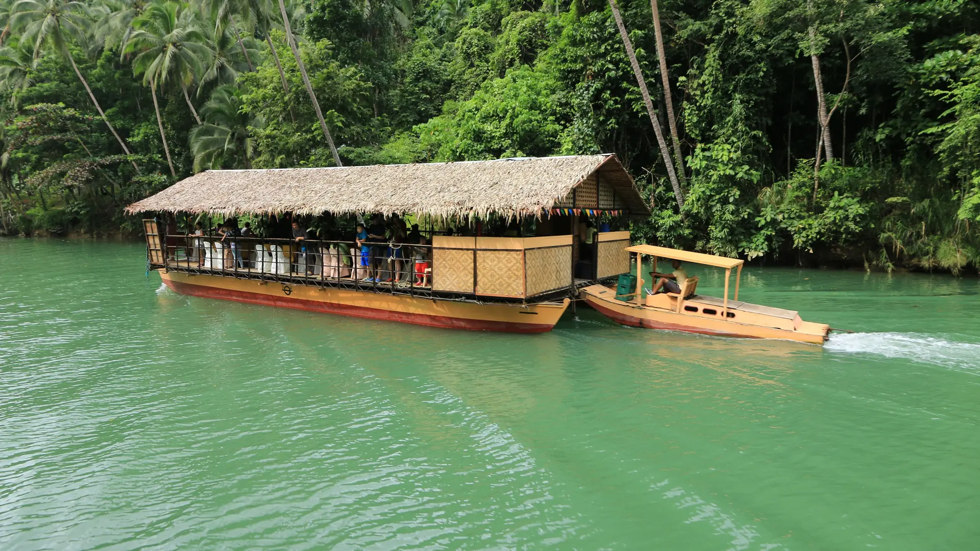 A thatched floating-restaurant raft on the green Loboc River between palm-covered banks
