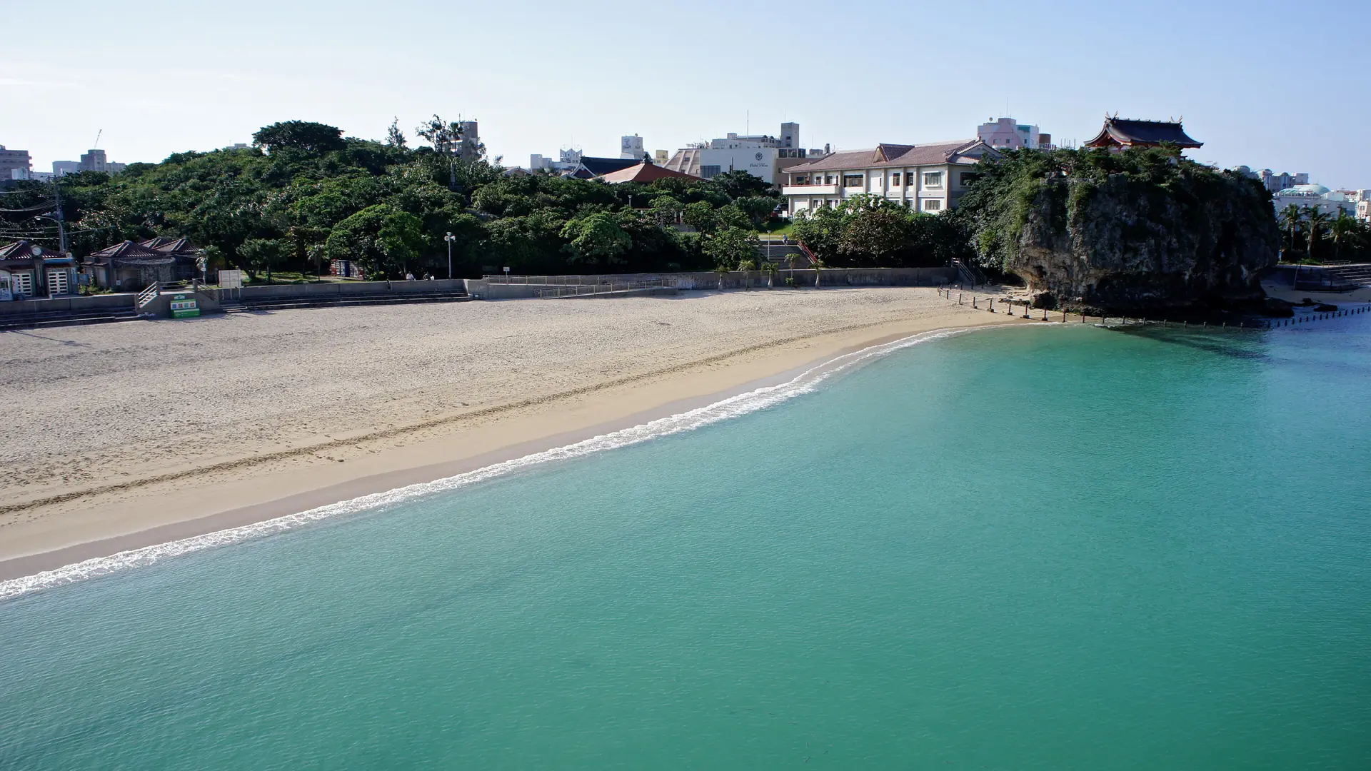 Sunlit sand and clear water at Naminoue Beach beneath Naha’s cliff-top shrine.