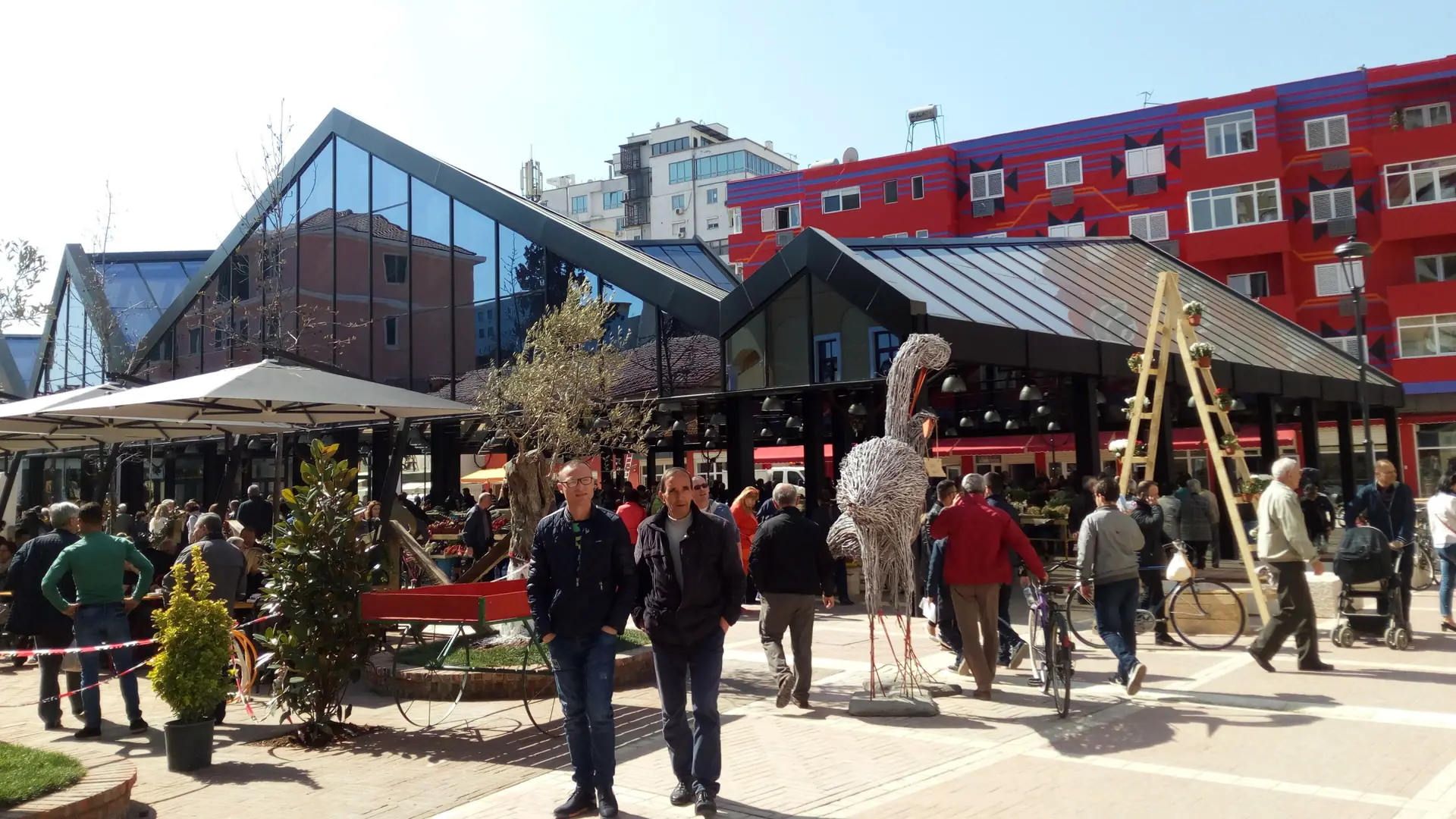 Shoppers outside the glass-roofed market hall of Tirana's New Bazaar on a bright day