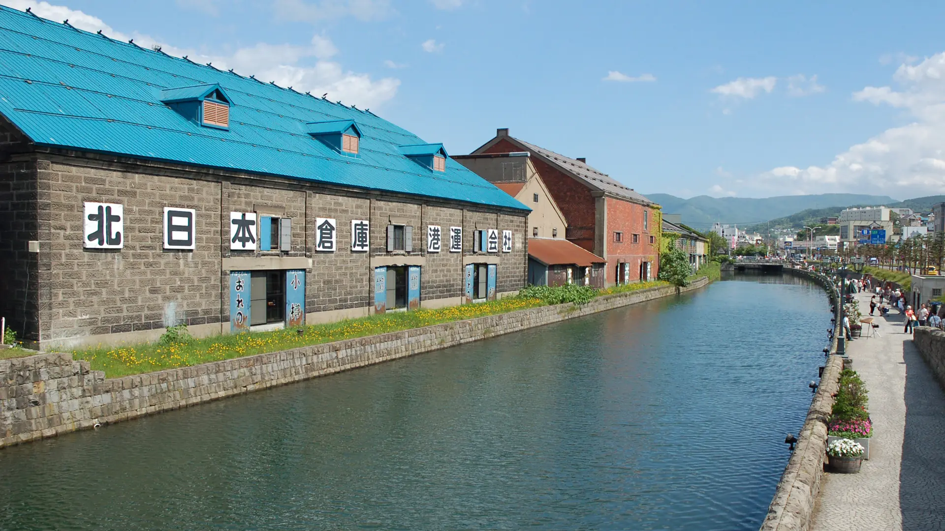 Stone warehouses and a pedestrian promenade beside Otaru Canal on a sunny day