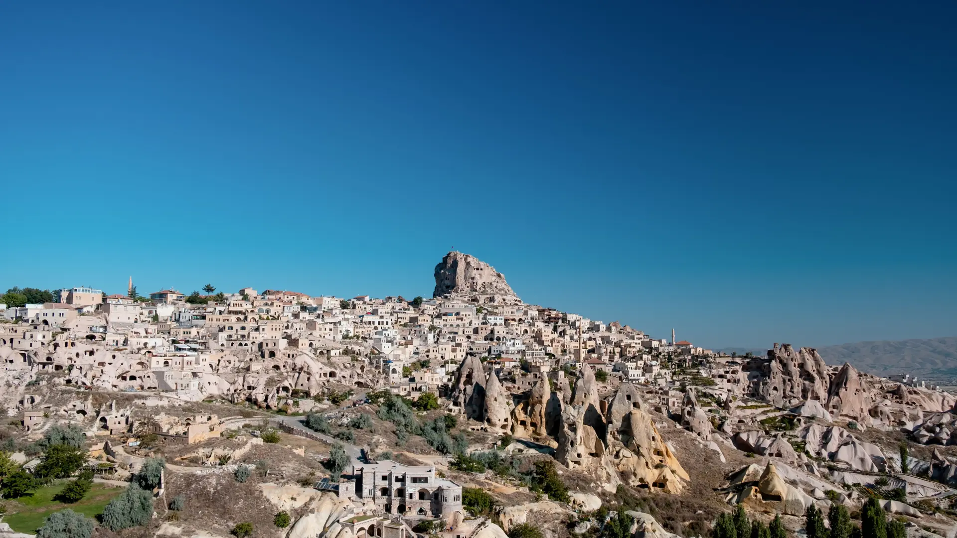 Sunny Uçhisar village and pale carved rocks, shown as a wider Cappadocia scene