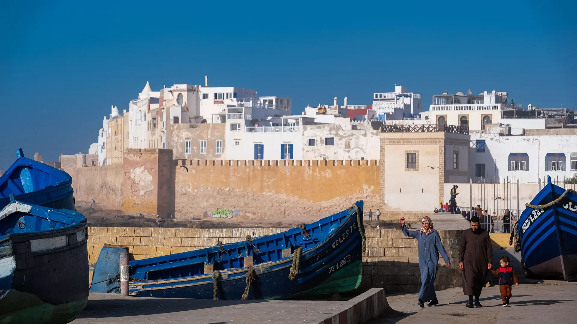Blue fishing boats beside Essaouira’s sunlit ramparts under a clear sky