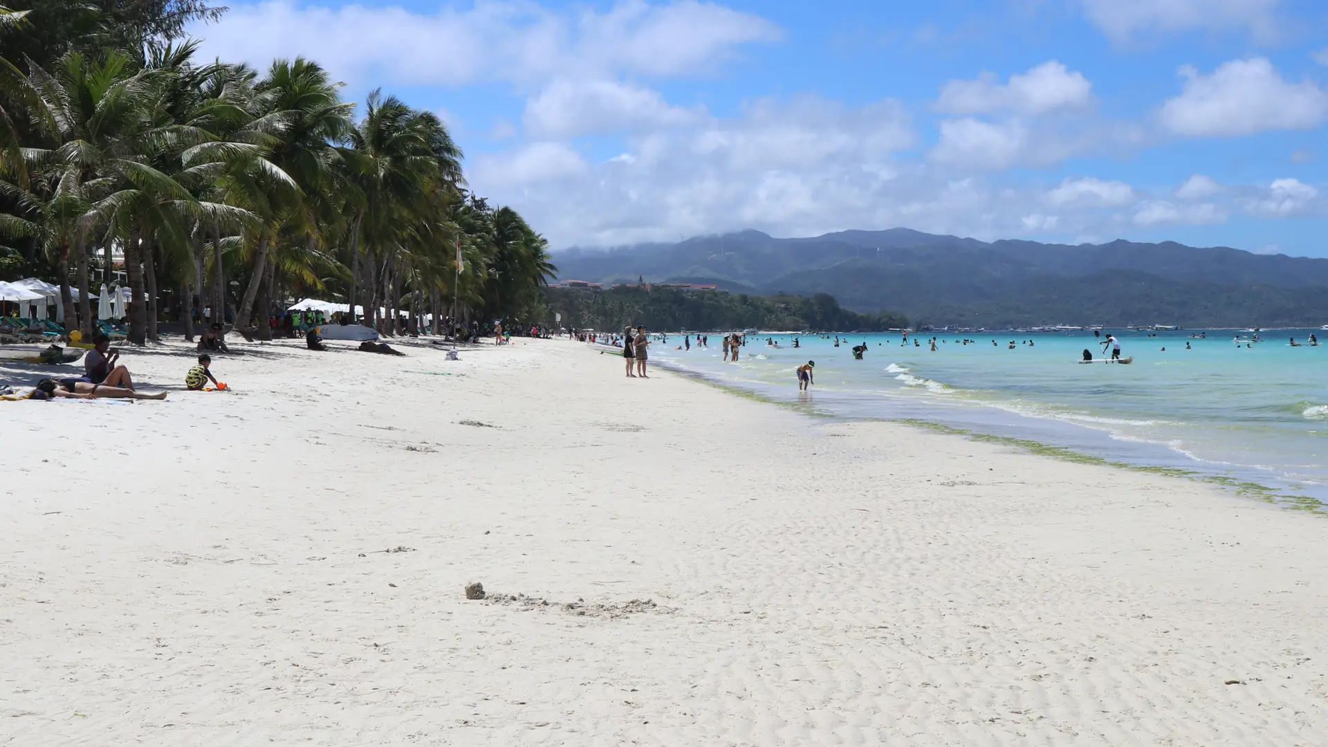 White sand, palms and swimmers on Boracay’s White Beach under a blue sky