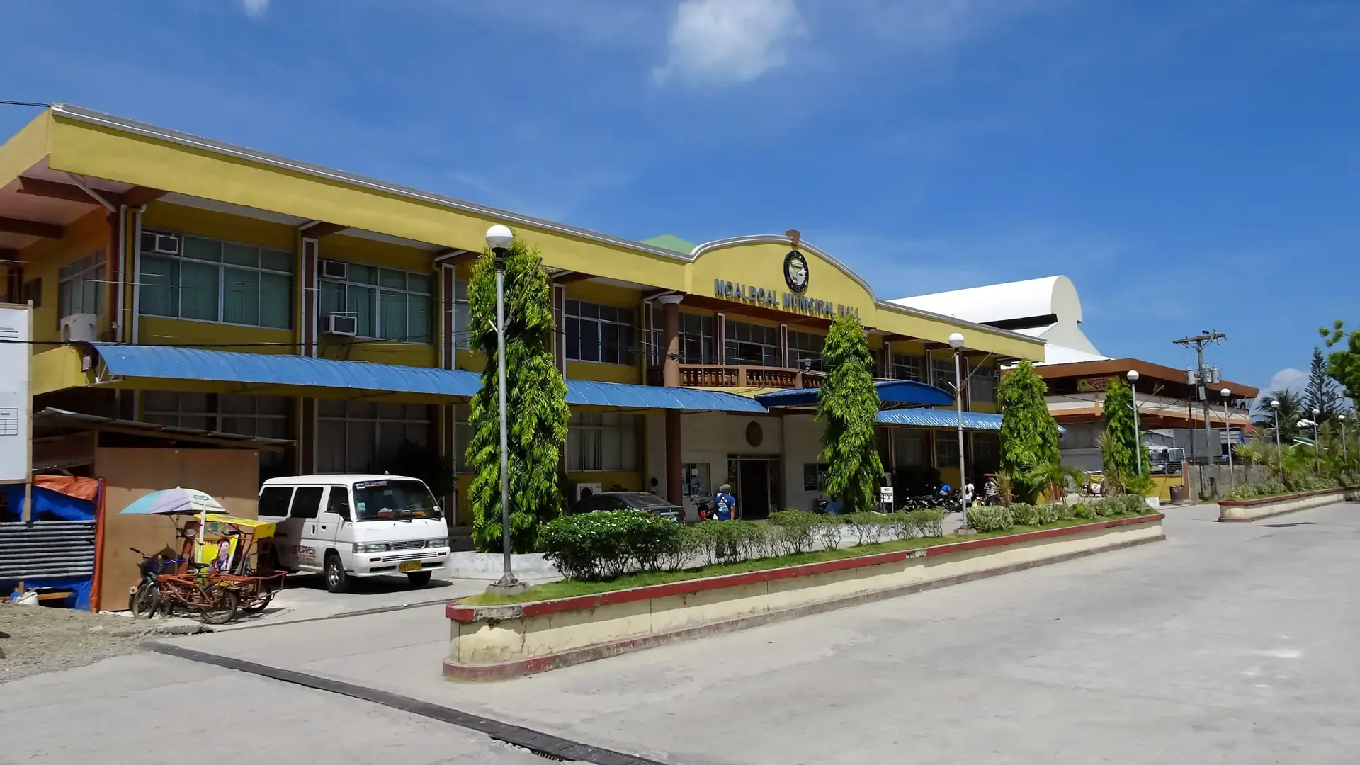 Moalboal Municipal Hall beside the town road, with blue awnings and trees under a bright sky
