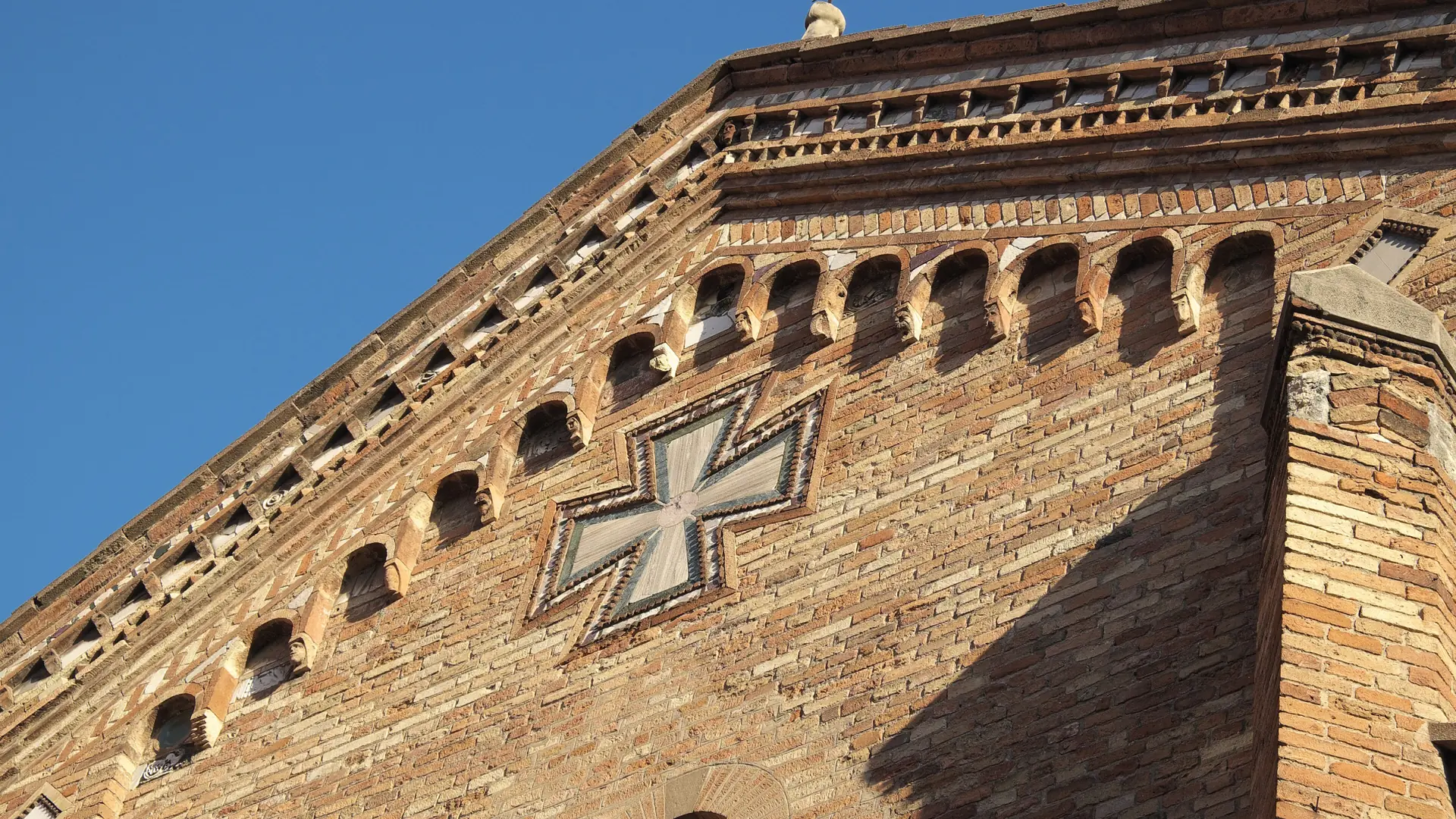 the Basilica di Santo Stefano's brick facade with a Maltese cross under a clear blue sky